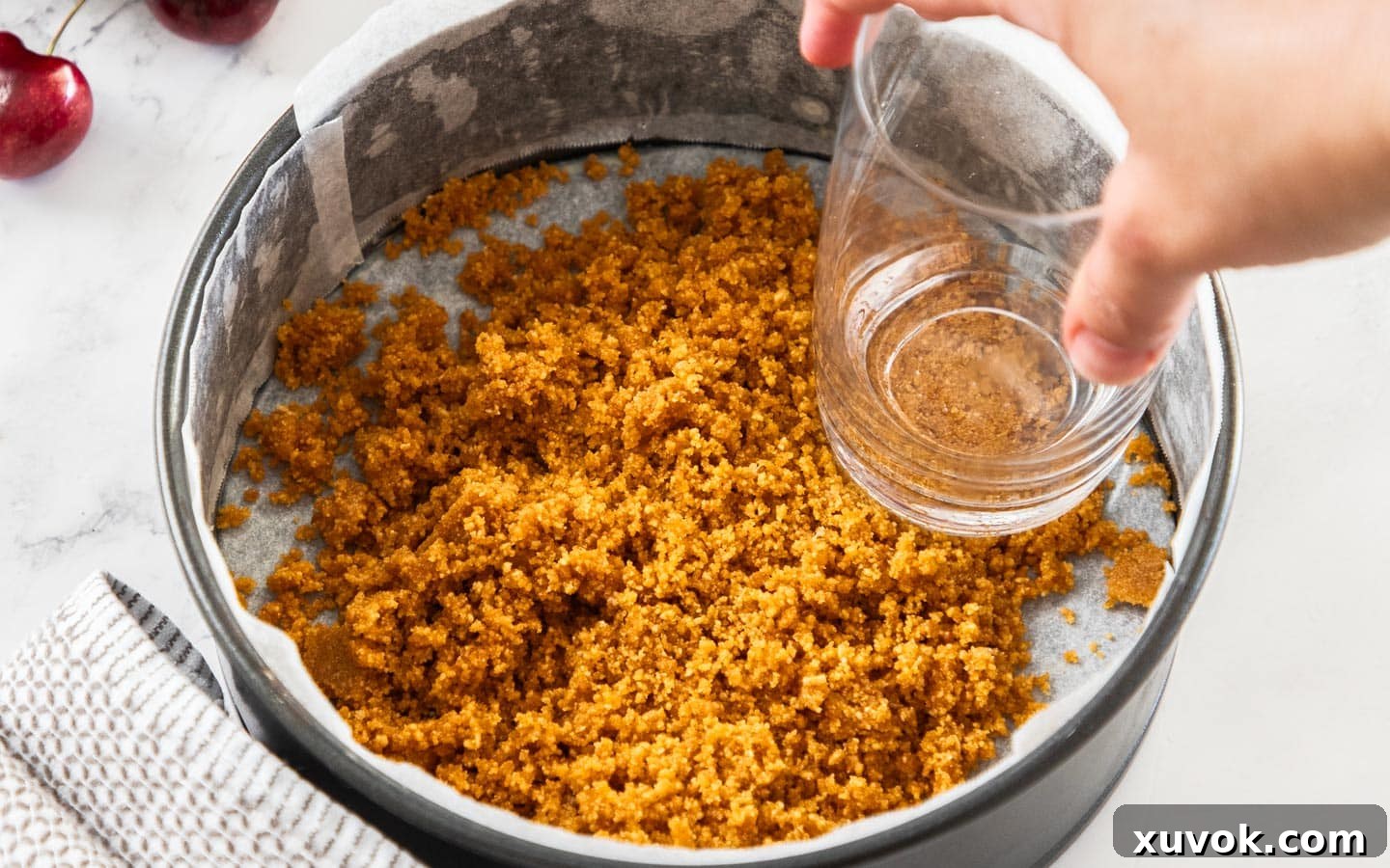 Crumbs being pressed into a pan with a glass.