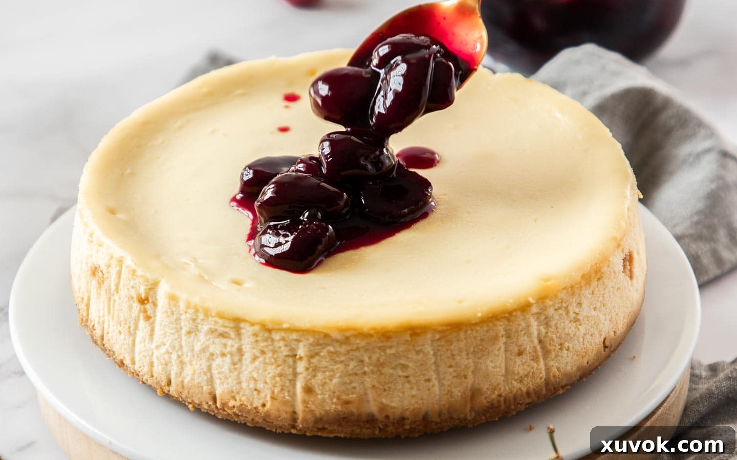 Cherry sauce being spooned onto the top of a cheesecake.