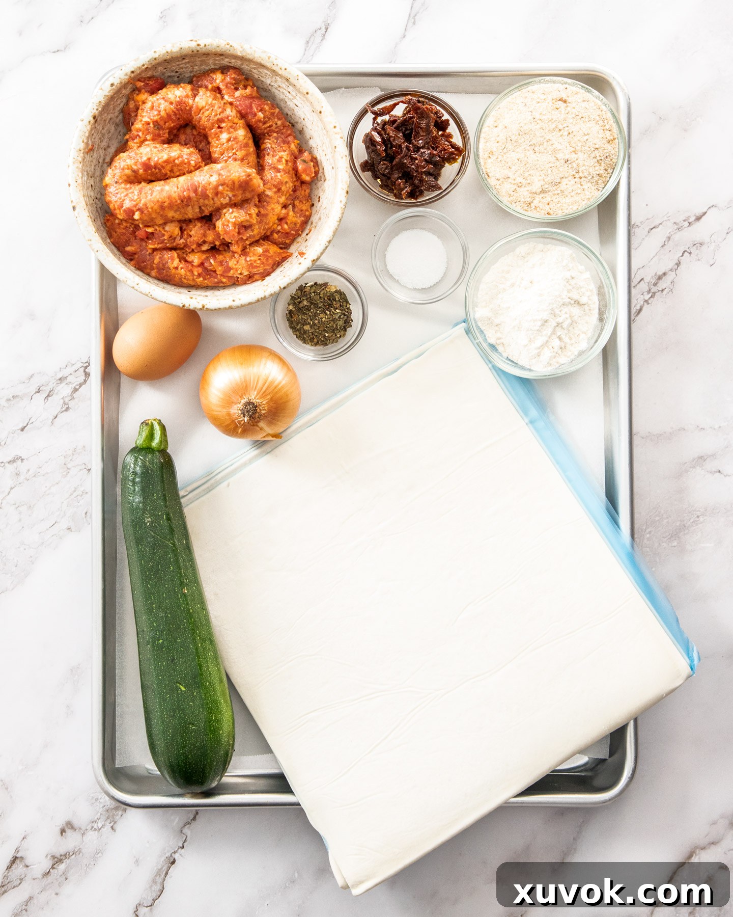 Ingredients for Italian sausage rolls laid out on a baking tray, ready for preparation.