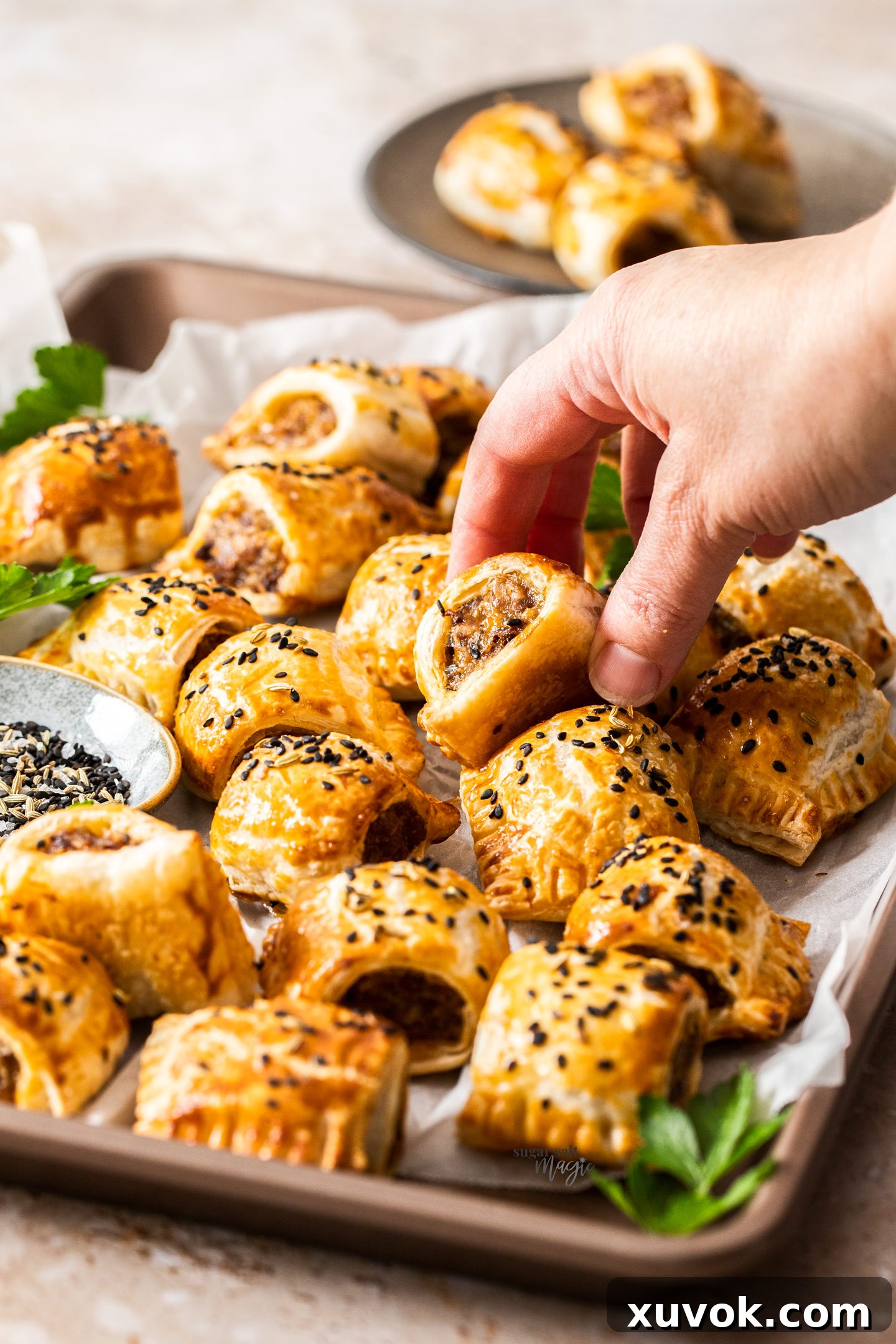 A hand reaching for a golden-brown Italian sausage roll from a baking tray, highlighting its irresistible appeal.