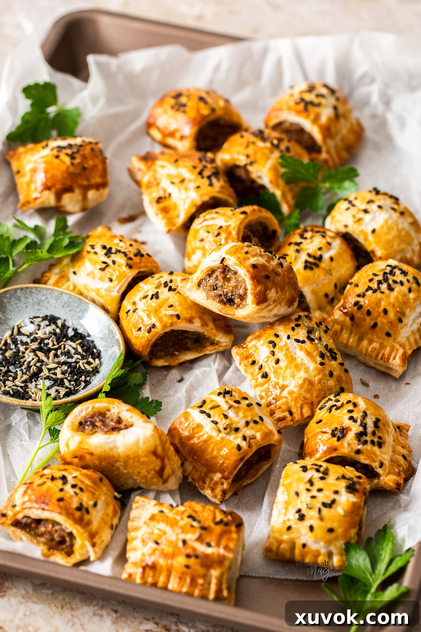 A batch of Italian sausage rolls cooling on a sheet of baking paper after being baked to a perfect golden crisp.