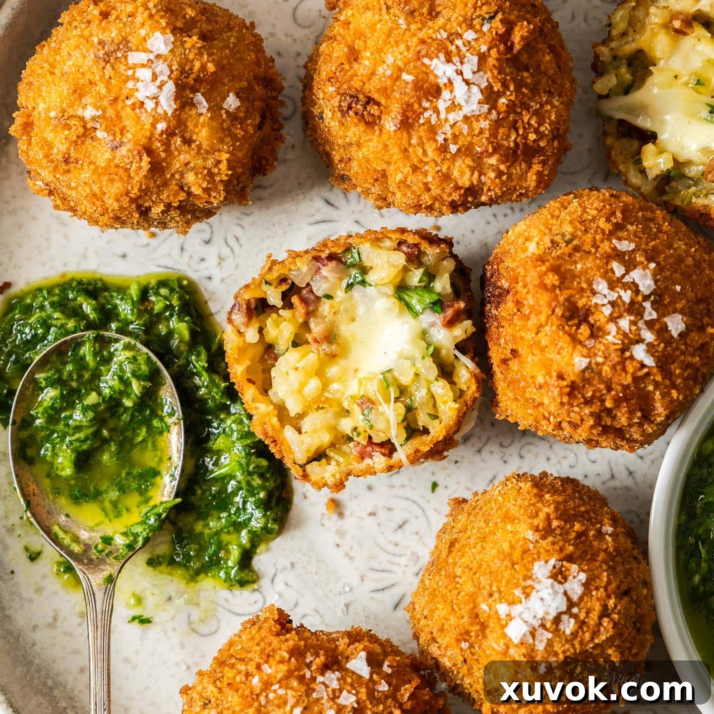 Top down view of a chorizo arancini ball cut in half showing the cheesy, rich interior, with a side of green mojo verde sauce for dipping.