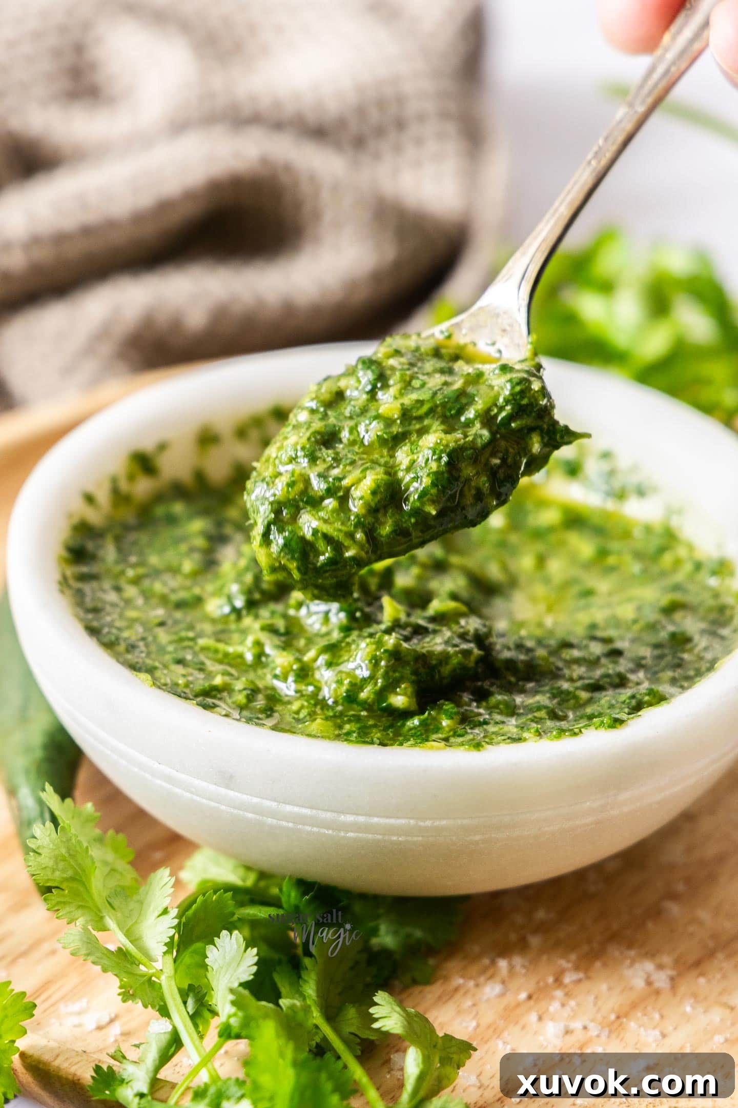 A close-up shot of a spoon scooping vibrant green mojo verde out of a rustic marble bowl, highlighting its fresh texture.
