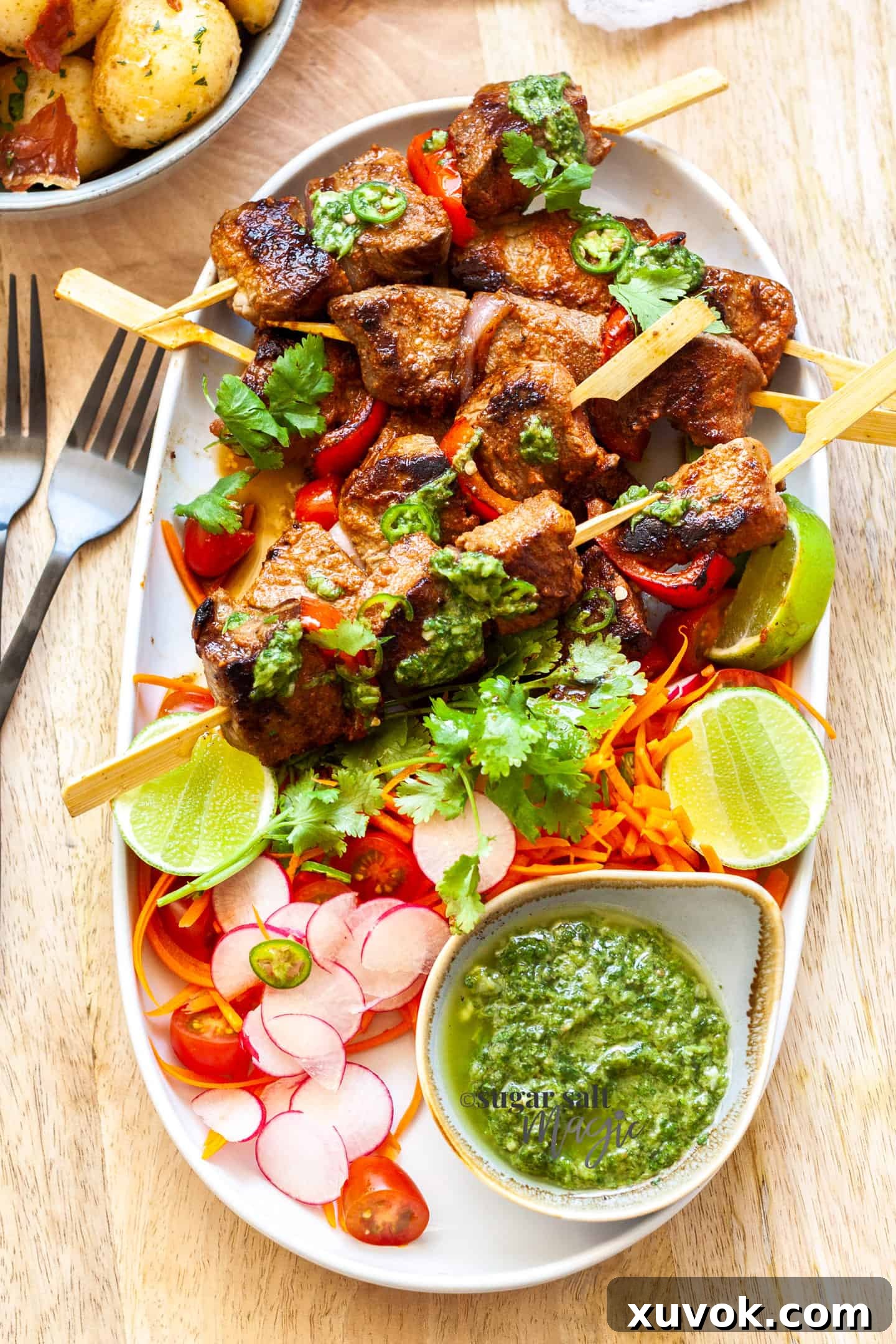 An oval dish filled with salad and steak kabobs with a green sauce, ready to be served.