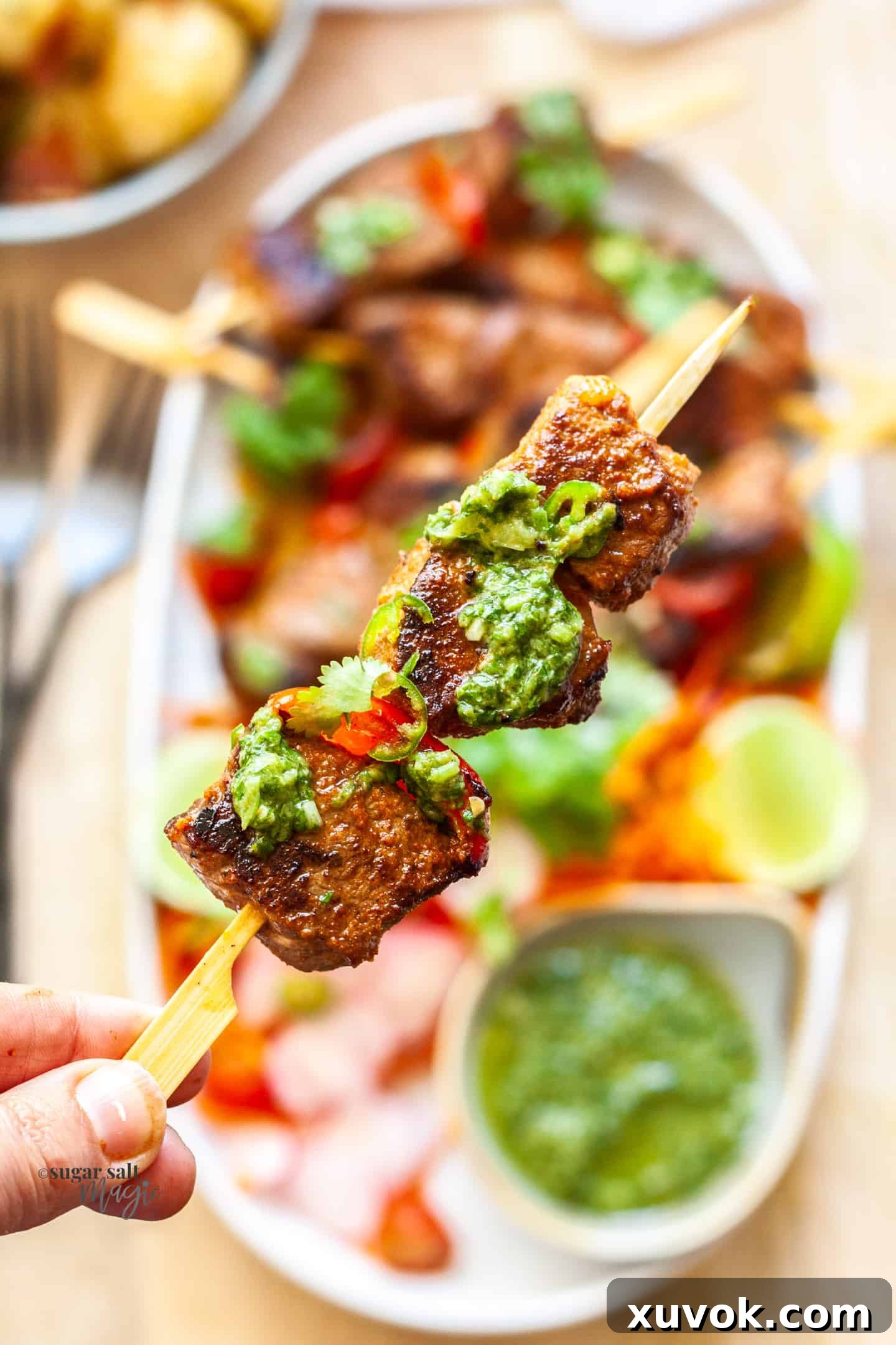 A hand holding a perfectly grilled shish kebab up to the camera, showcasing the charred meat and vegetables.