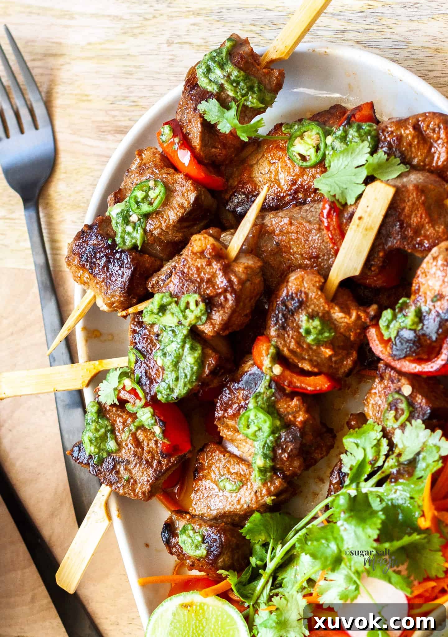 Top down view of steak kabobs beautifully arranged on a platter with a vibrant green sauce drizzled over them.