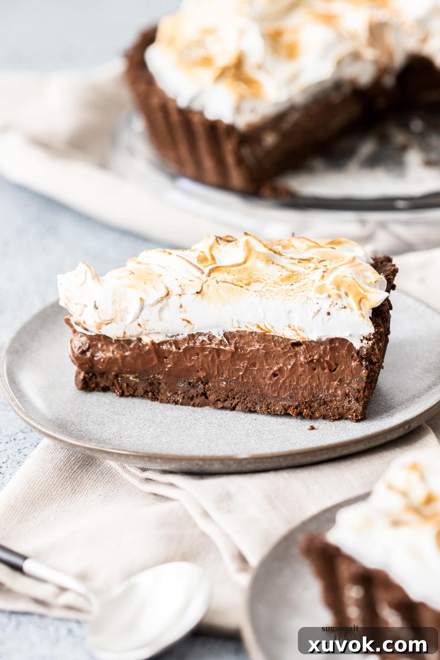 A perfectly portioned slice of chocolate meringue pie, revealing its distinct layers of cookie crust, chocolate custard, and marshmallow meringue, served on a dessert plate.