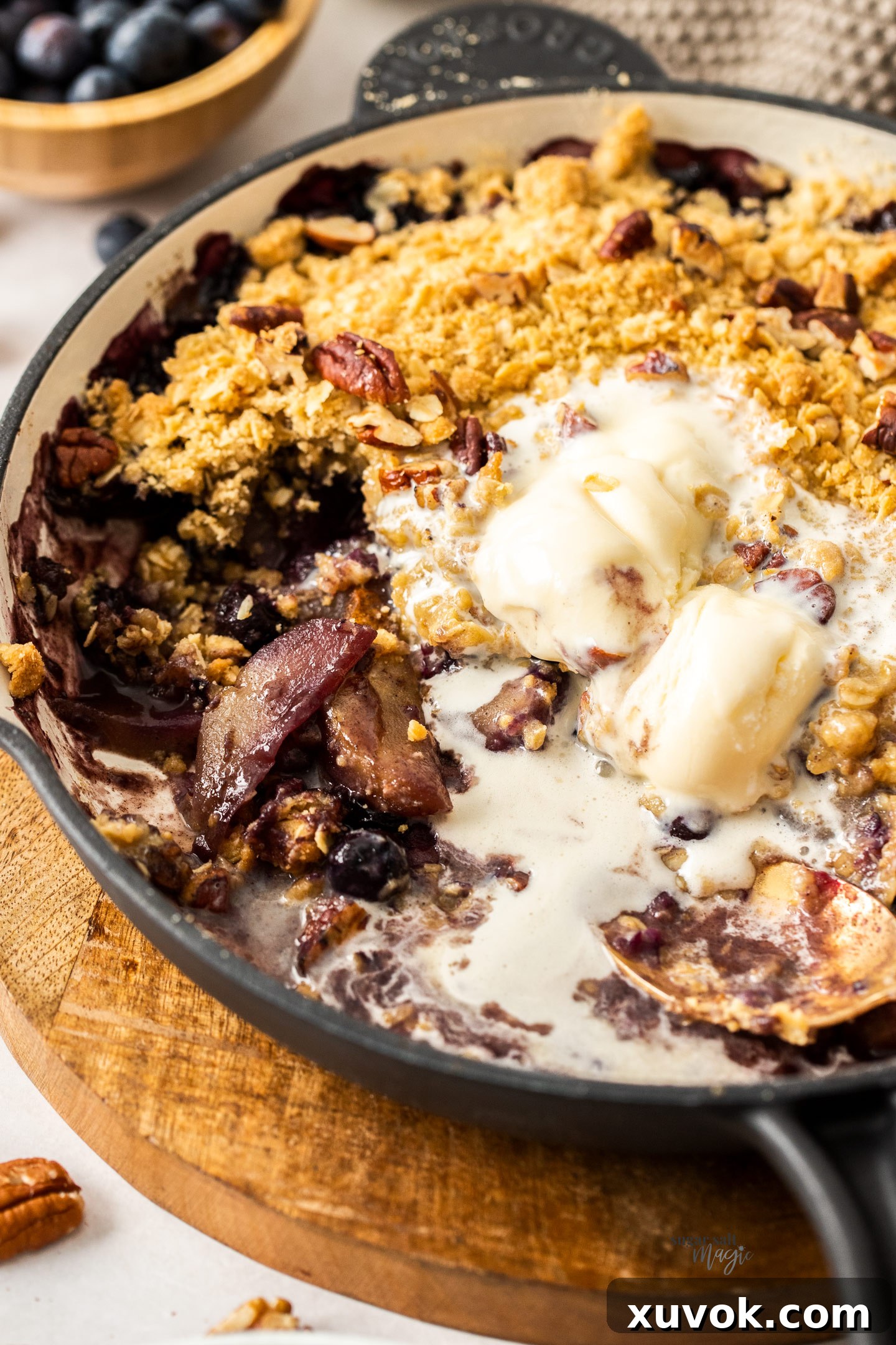 Closeup of the baked pear and blueberry filling, showing the softened fruit and bubbling juices beneath the golden crumble topping.