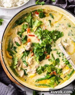 A large skillet filled with green chicken curry. A mouthwatering close-up of a large skillet brimming with freshly cooked Thai Green Chicken Curry, featuring tender chicken pieces and vibrant vegetables submerged in a rich, green coconut sauce.