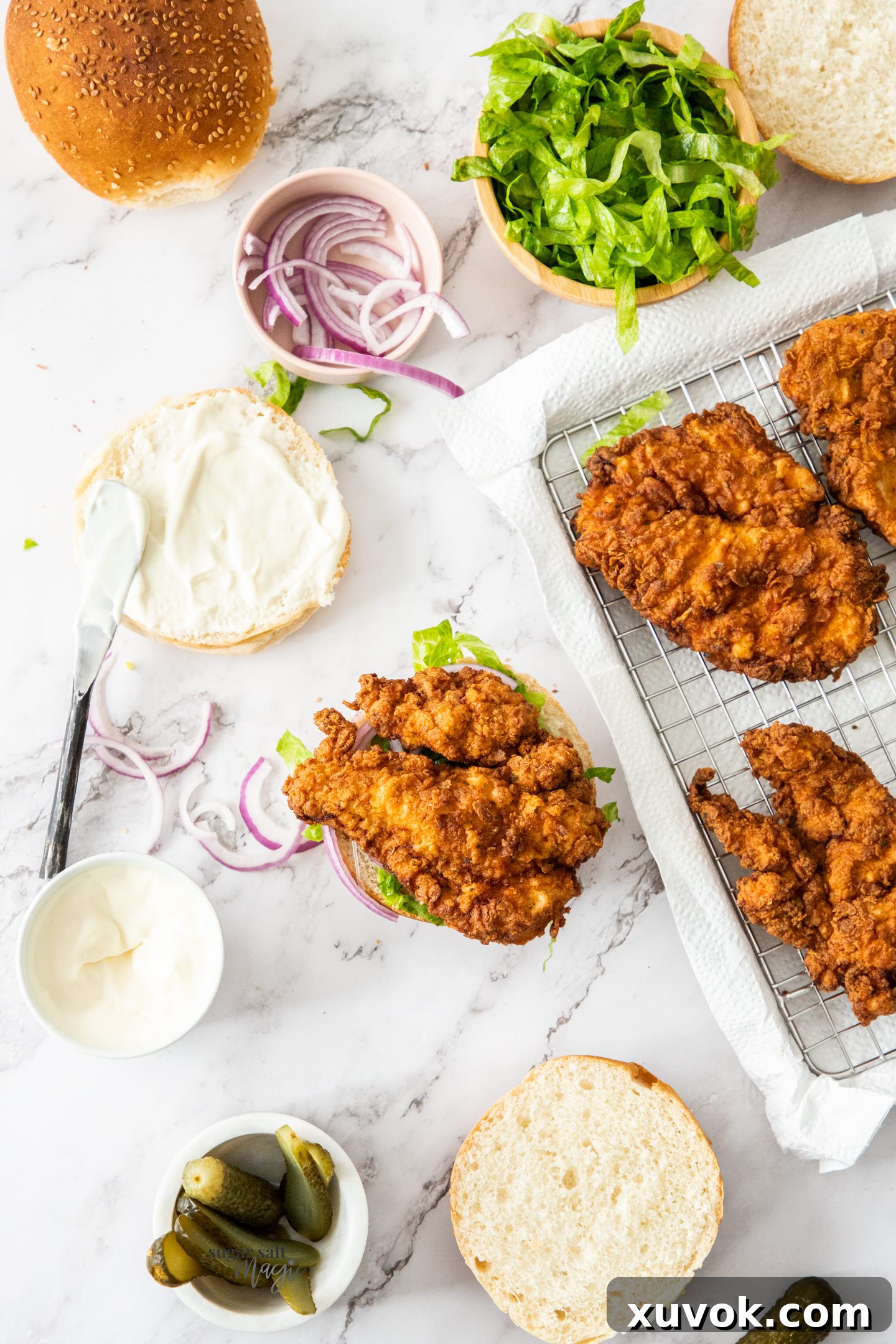 A chicken burger assembly station with buns, crispy chicken, and fresh salad components.