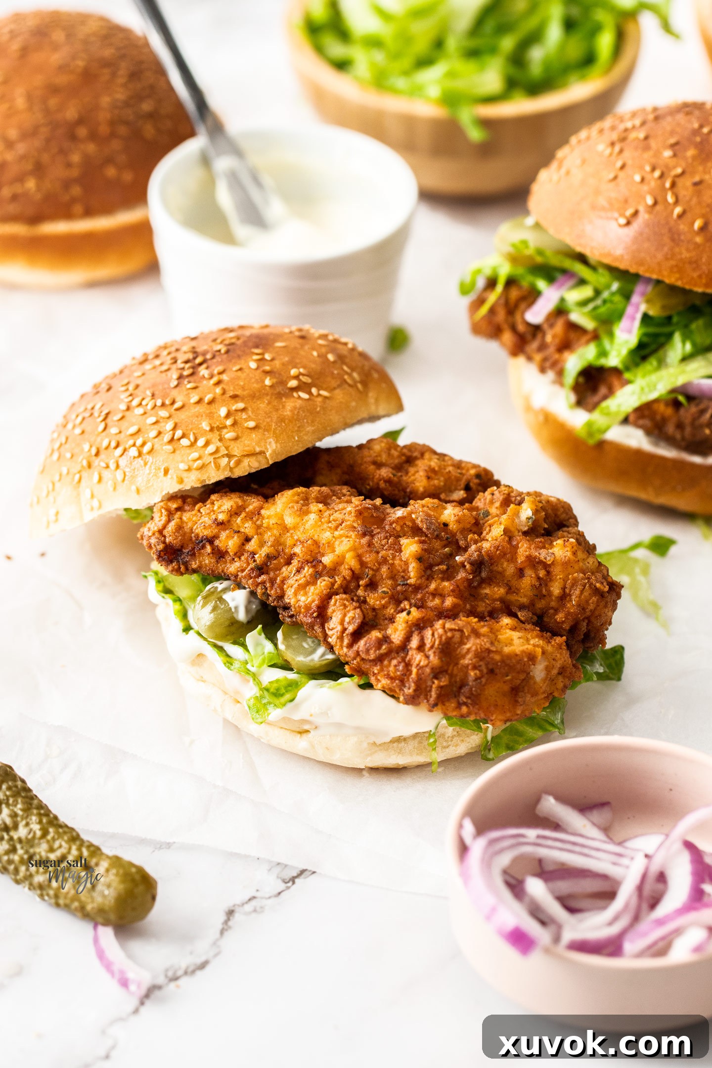 A perfectly assembled fried chicken burger with its top bun casually placed beside it.