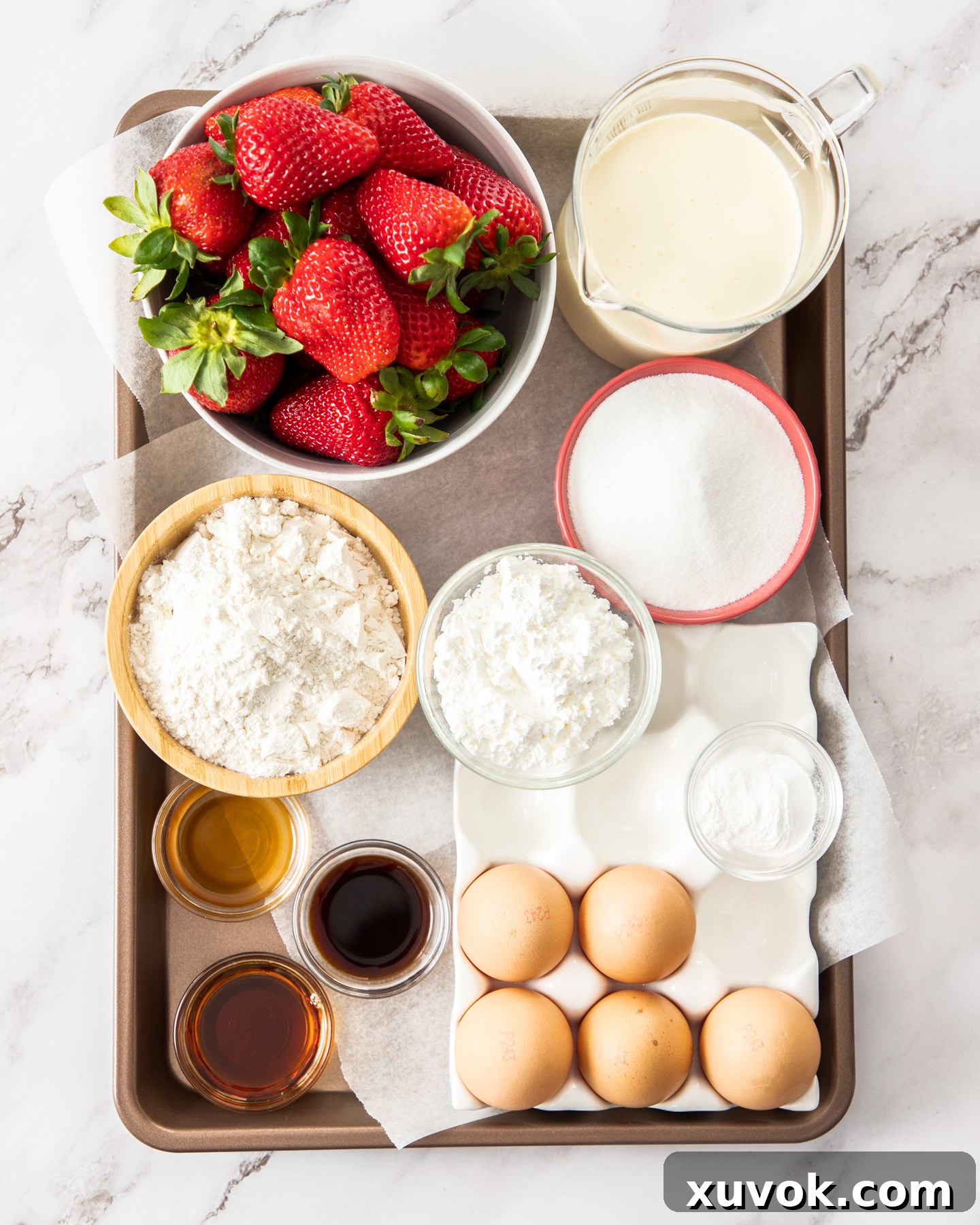 Ingredients for strawberry sponge cake laid out on a baking tray, highlighting freshness.