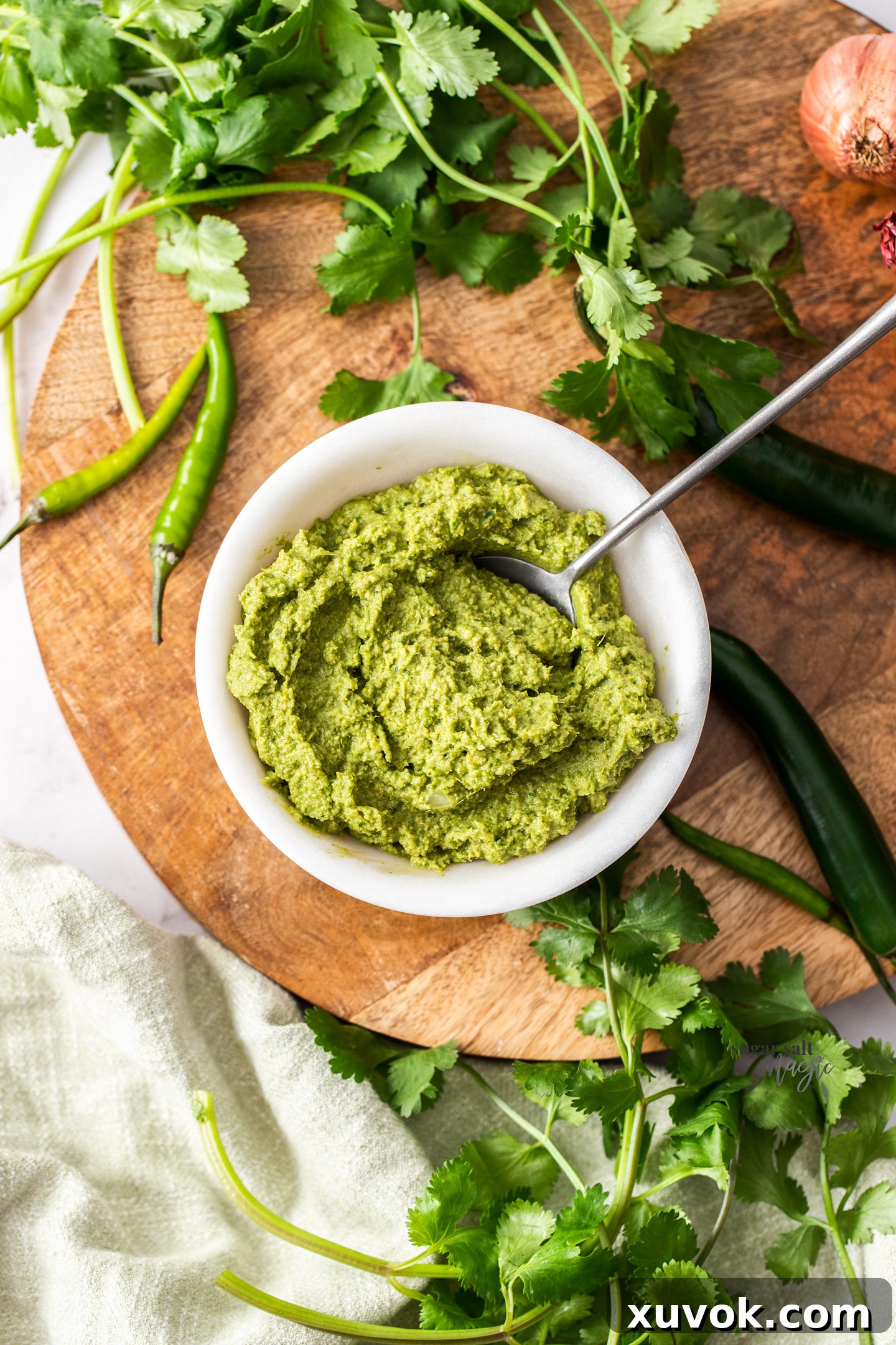 Homemade Thai green curry paste in a marble bowl with fresh ingredients like green chillies, coriander, and lemongrass artfully arranged around it.