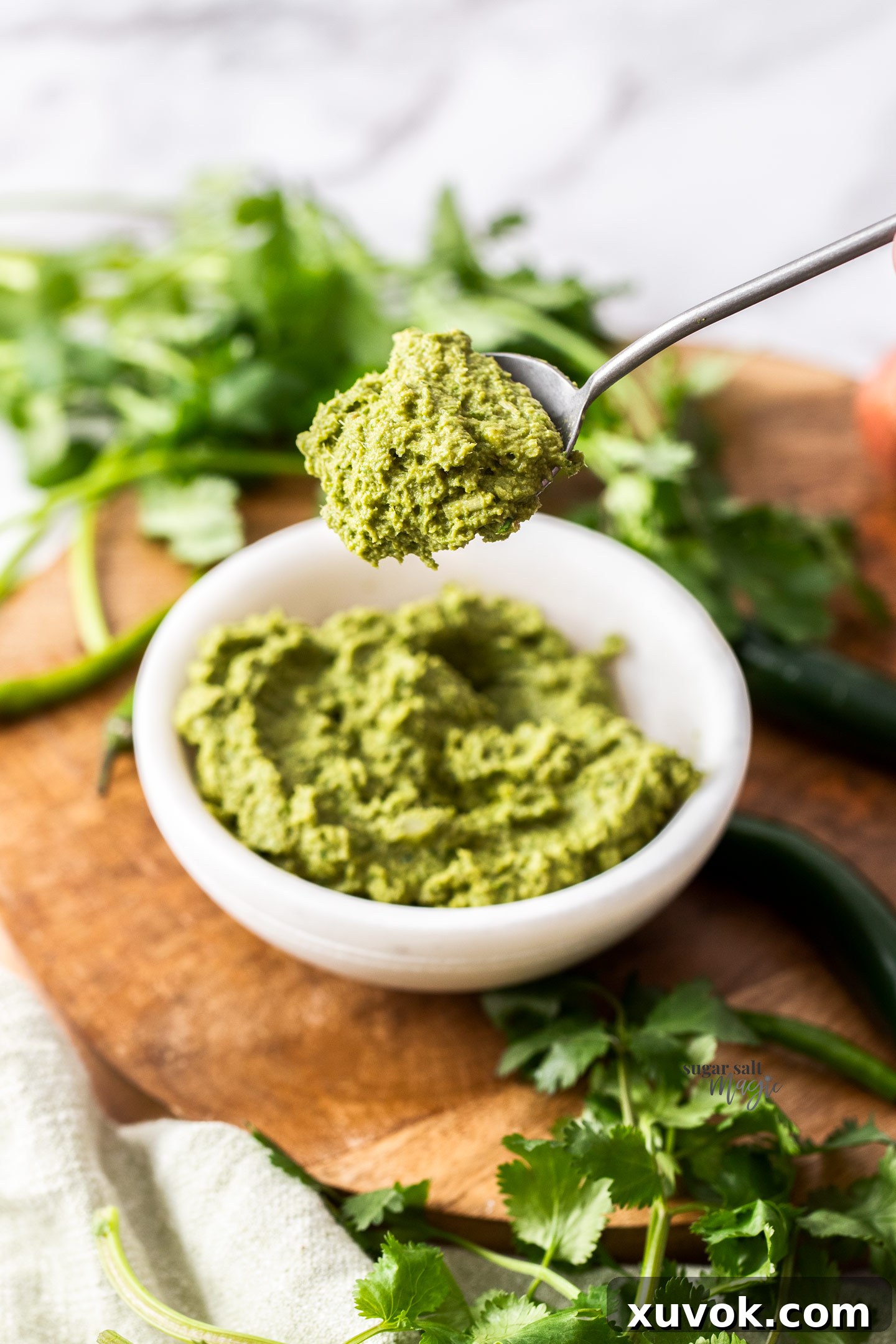 A spoon scooping a portion of rich green curry paste from a marble bowl, highlighting its texture.