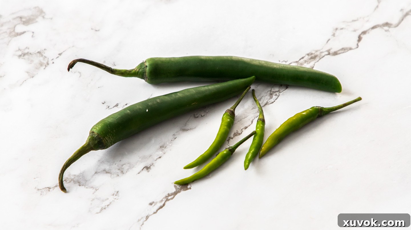 A variety of green chillies, including small hot Thai green chillies and larger long green chillies, displaying different heat levels.
