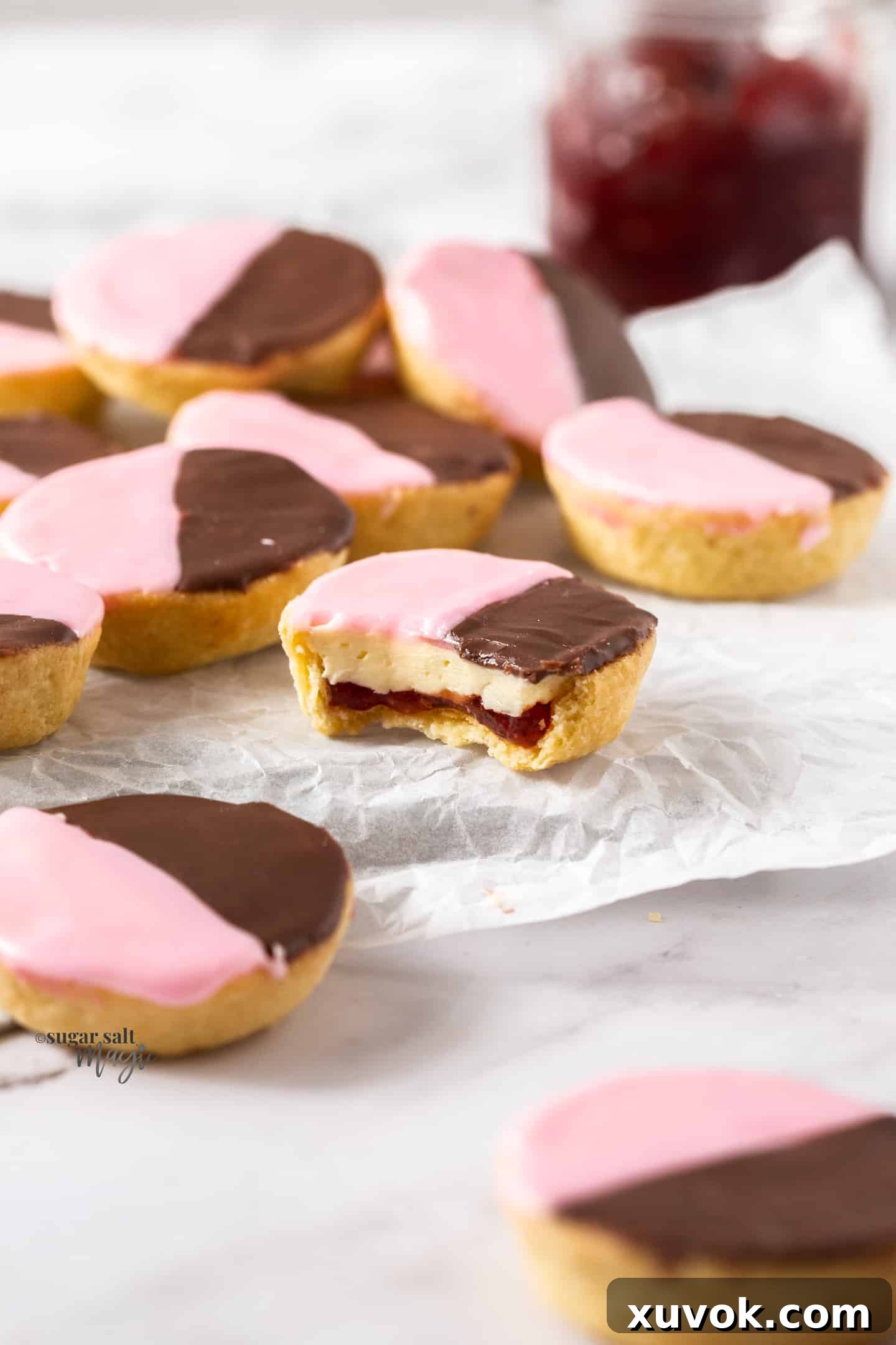 A close-up view of a Neenish tart cut in half, revealing the layers of golden pastry, vibrant jam, and creamy white mock cream inside, all topped with the characteristic two-tone icing.