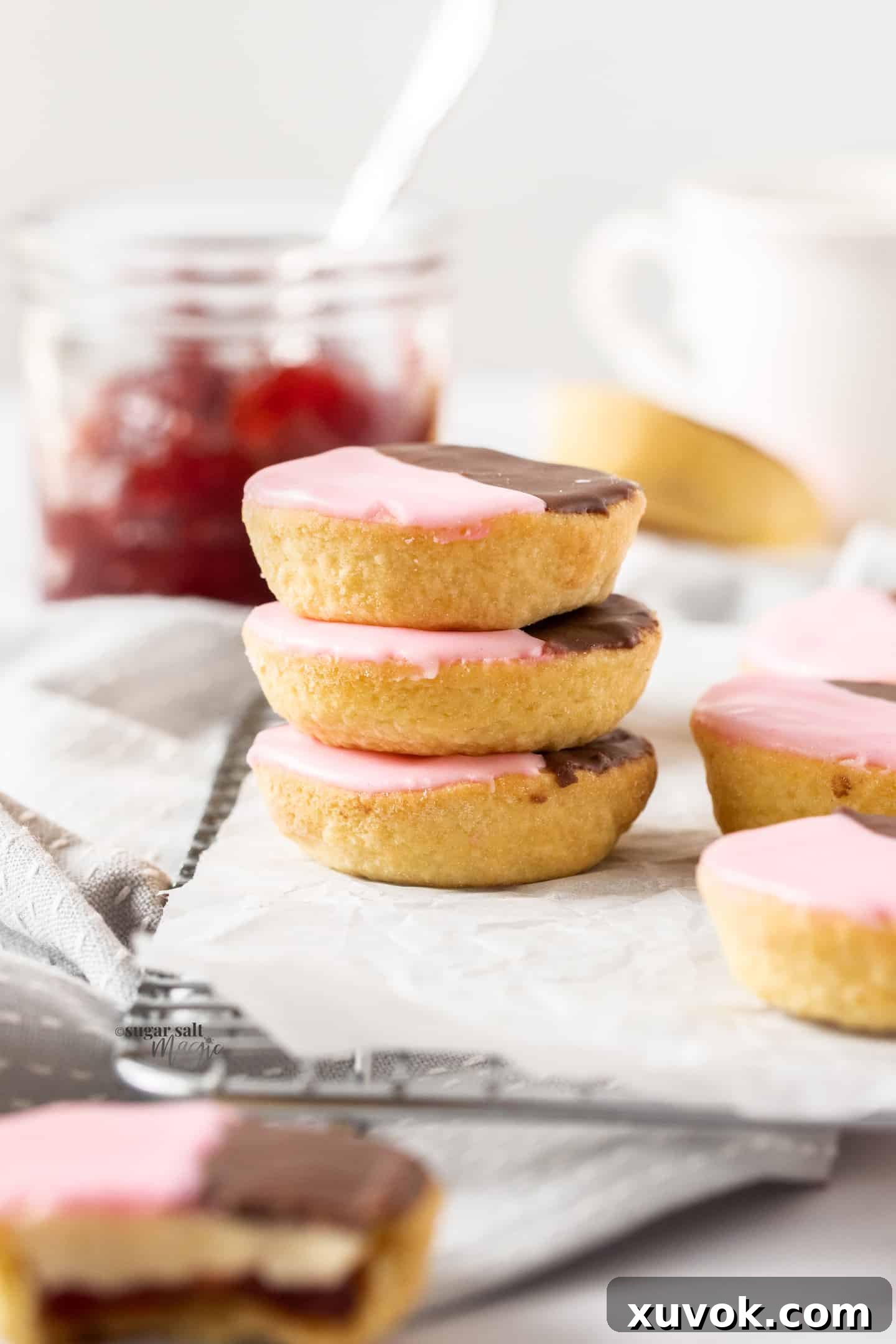 A beautiful stack of three traditional Neenish tarts sits on a wire cooling rack, with a rustic jar of fruit jam subtly blurred in the background, hinting at the delicious filling.