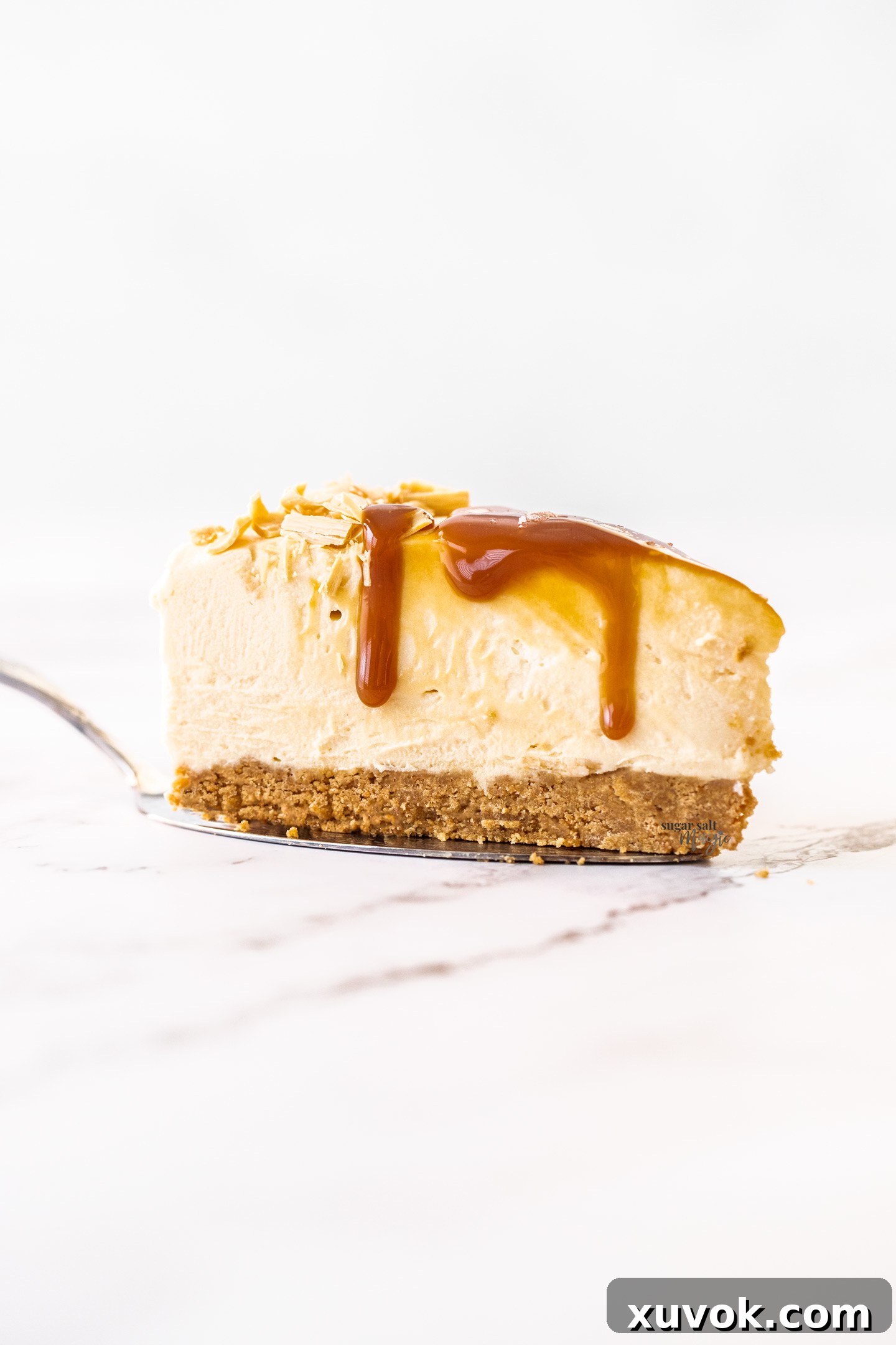 A perfectly sliced piece of creamy Caramilk cheesecake on a spatula, ready to be served, showcasing its smooth texture and golden hue.