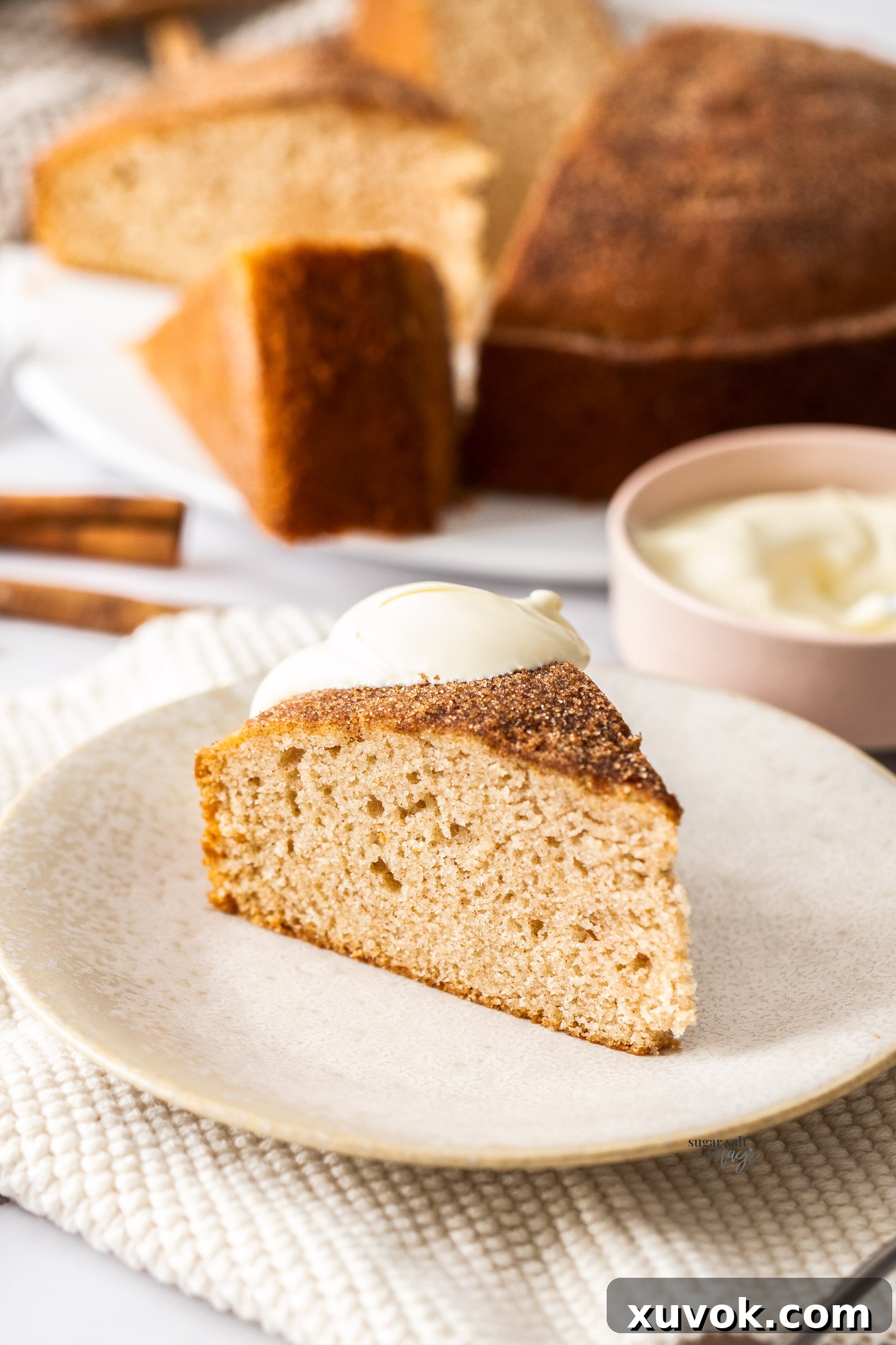 A delicious slice of cinnamon teacake artfully presented on a small plate, garnished with a dollop of fresh cream and a sprig of mint, ready to be enjoyed.
