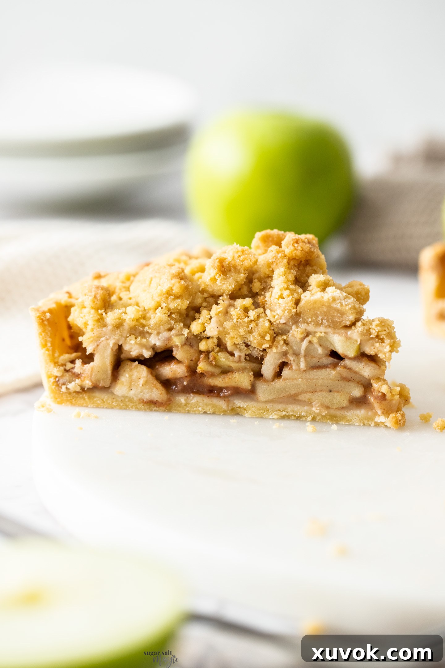 A perfectly baked apple crumble tart, with a golden brown streusel topping and a rich filling, sits on a white marble platter, emphasizing its rustic elegance.
