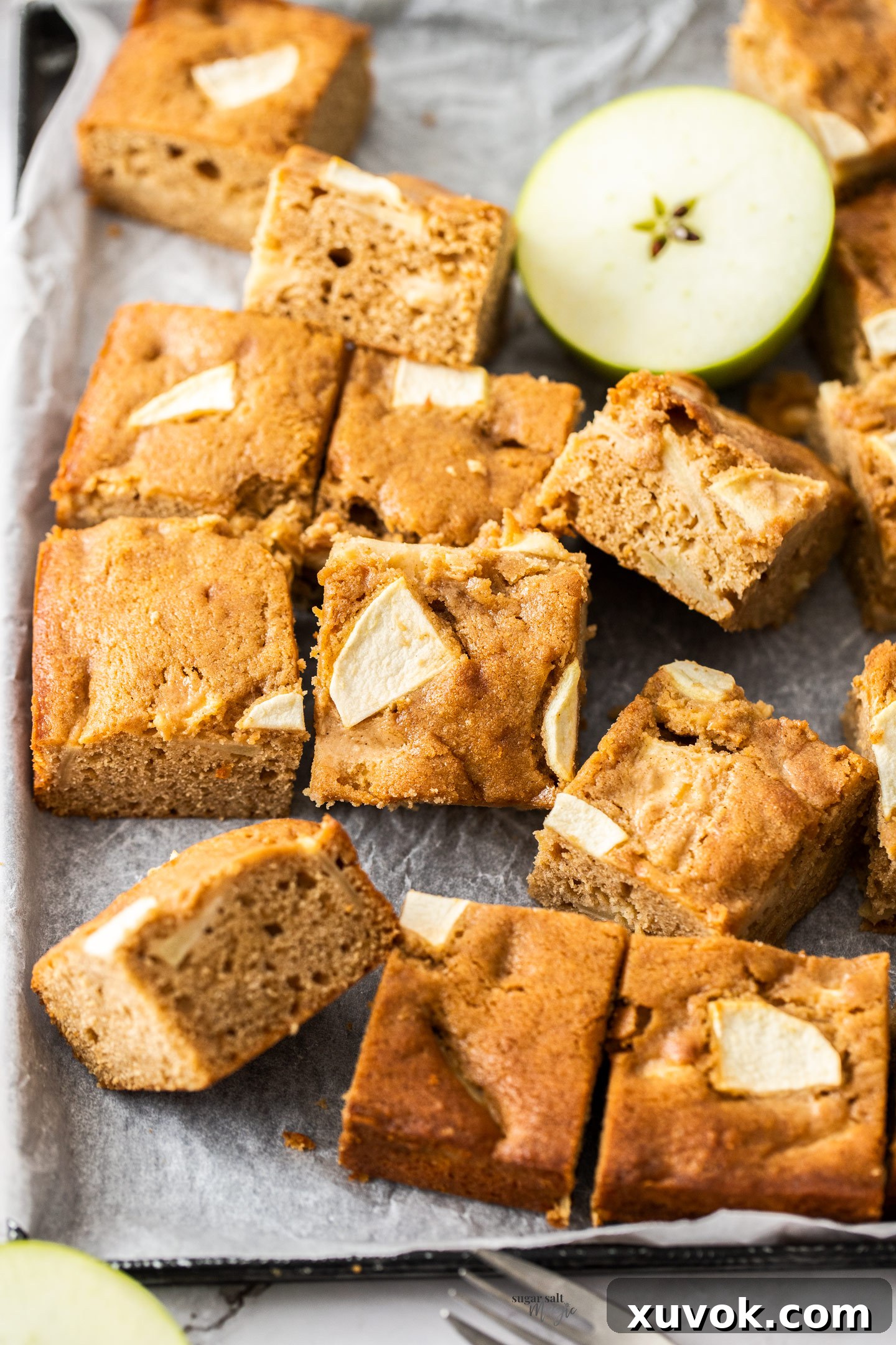 Beautifully sliced squares of apple cake arranged on a serving plate with a fresh apple in the background, showcasing its golden-brown crust and moist interior.