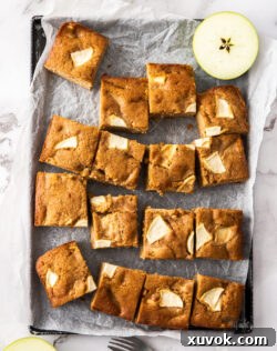 An inviting image of a freshly baked apple tray bake cake, cut into perfect squares and presented on a baking tray.