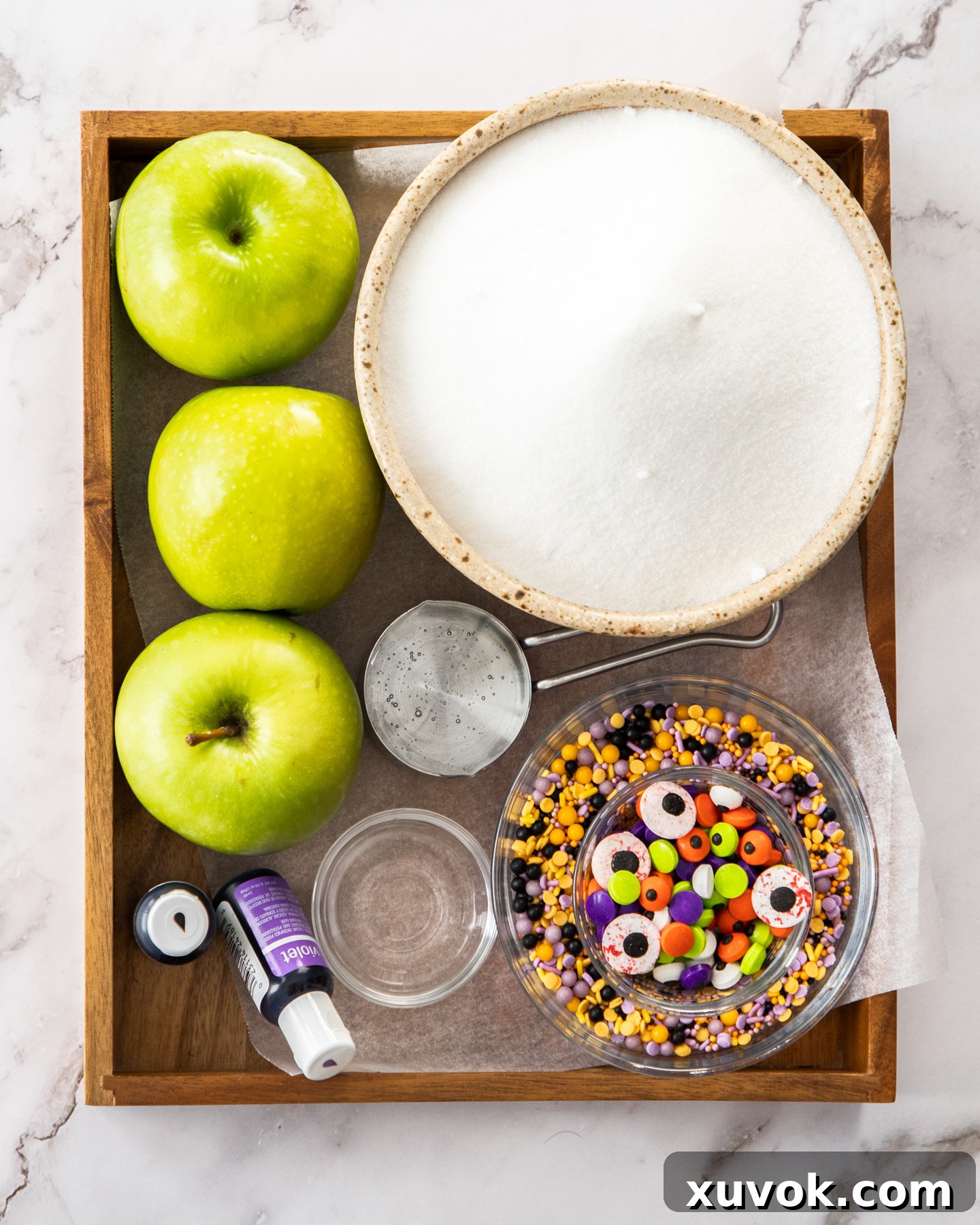 Ingredients for halloween candy apples on a wooden tray.