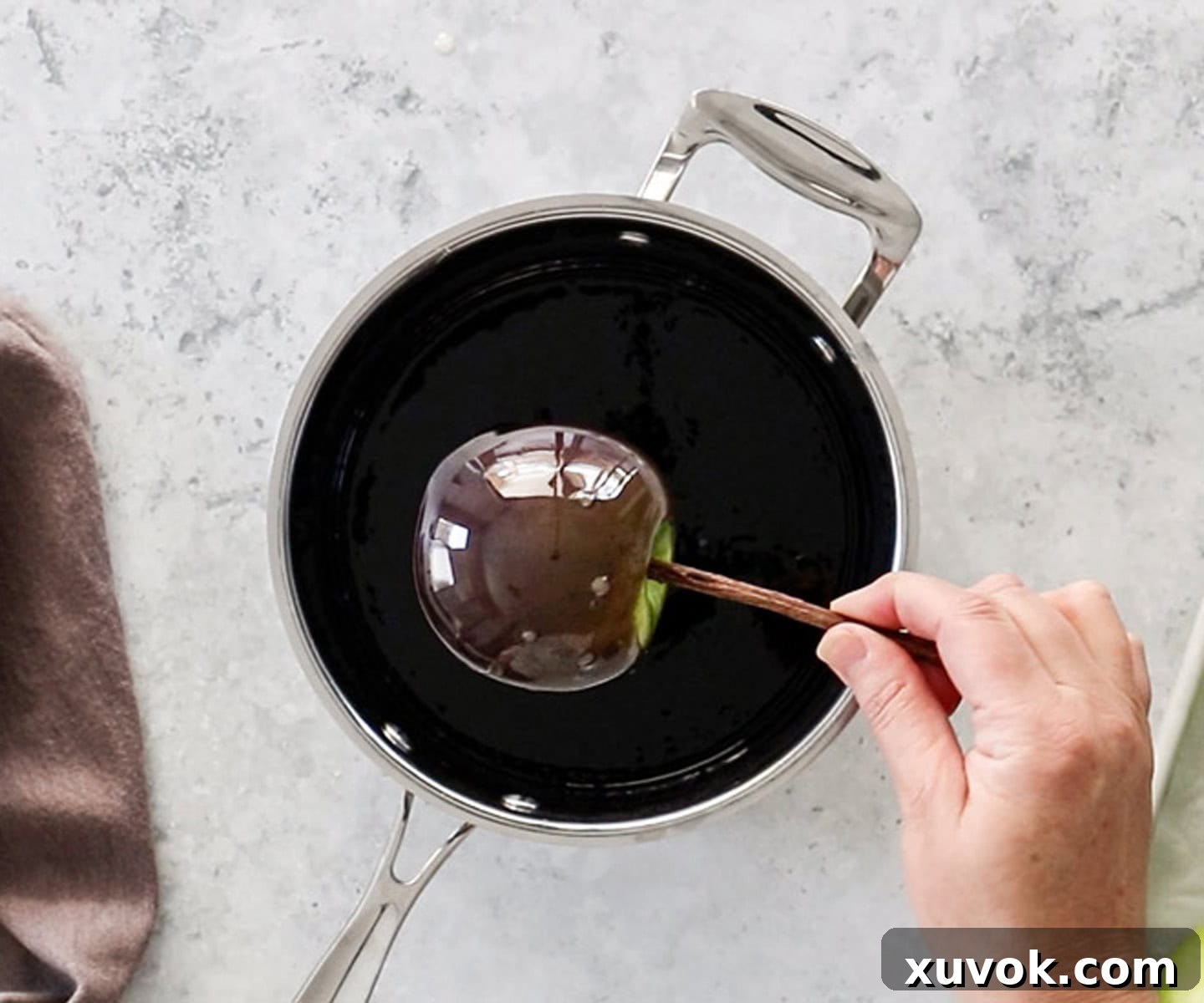 An apple on a stick being coated in black toffee from a pan.