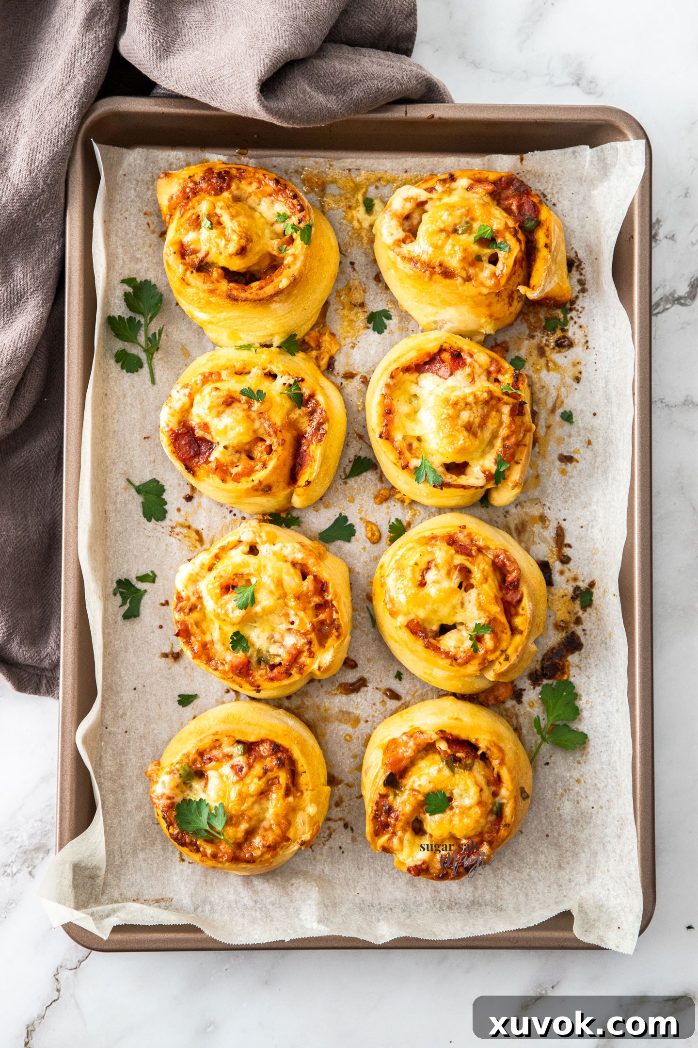 Eight golden-brown pizza scrolls neatly arranged on a baking tray, showcasing their perfect swirl and appetizing crust.