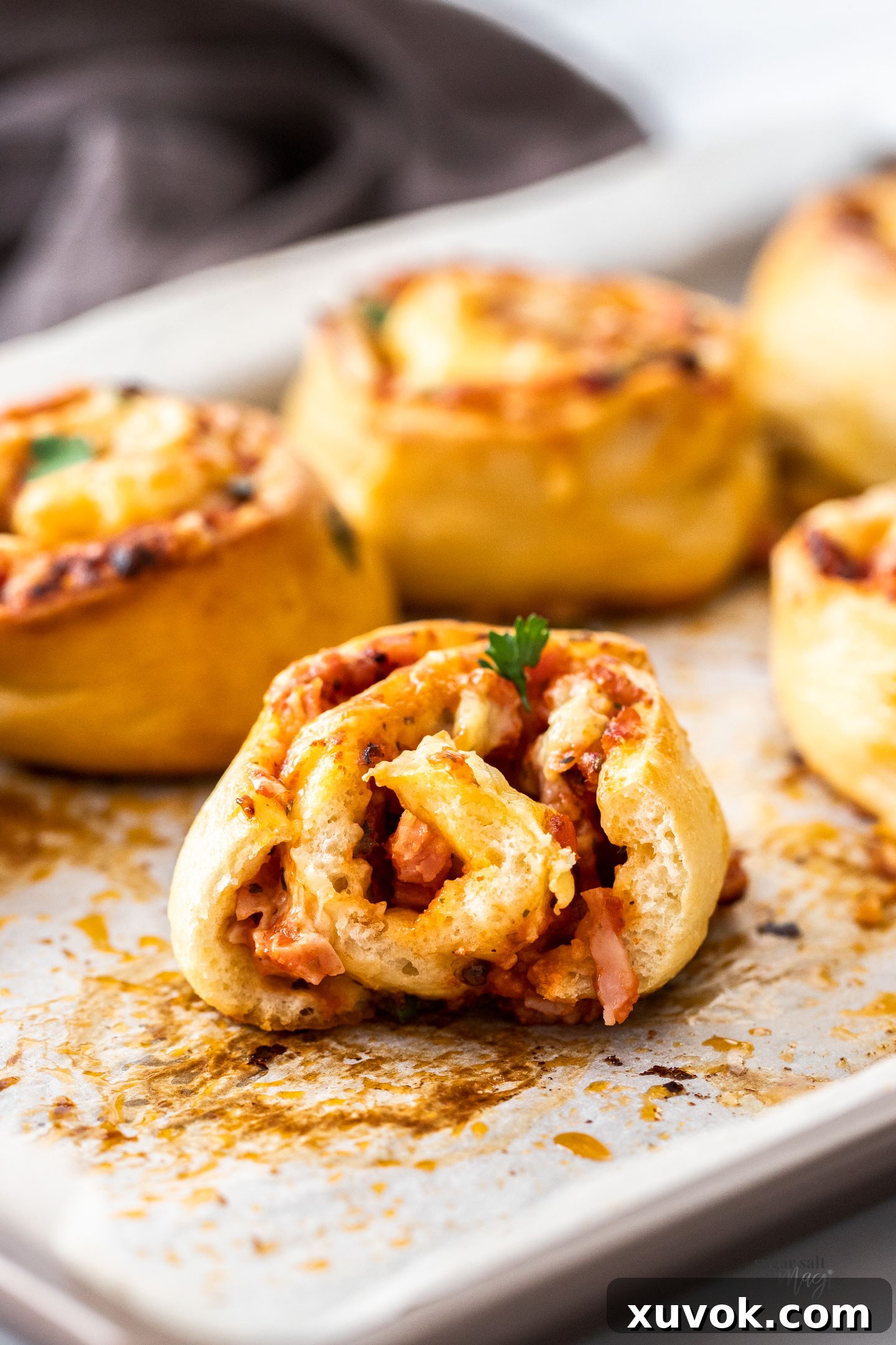 A baked pizza scroll is torn open, revealing the soft, fluffy interior of the dough, the melted cheese, and the ham and sauce swirl.