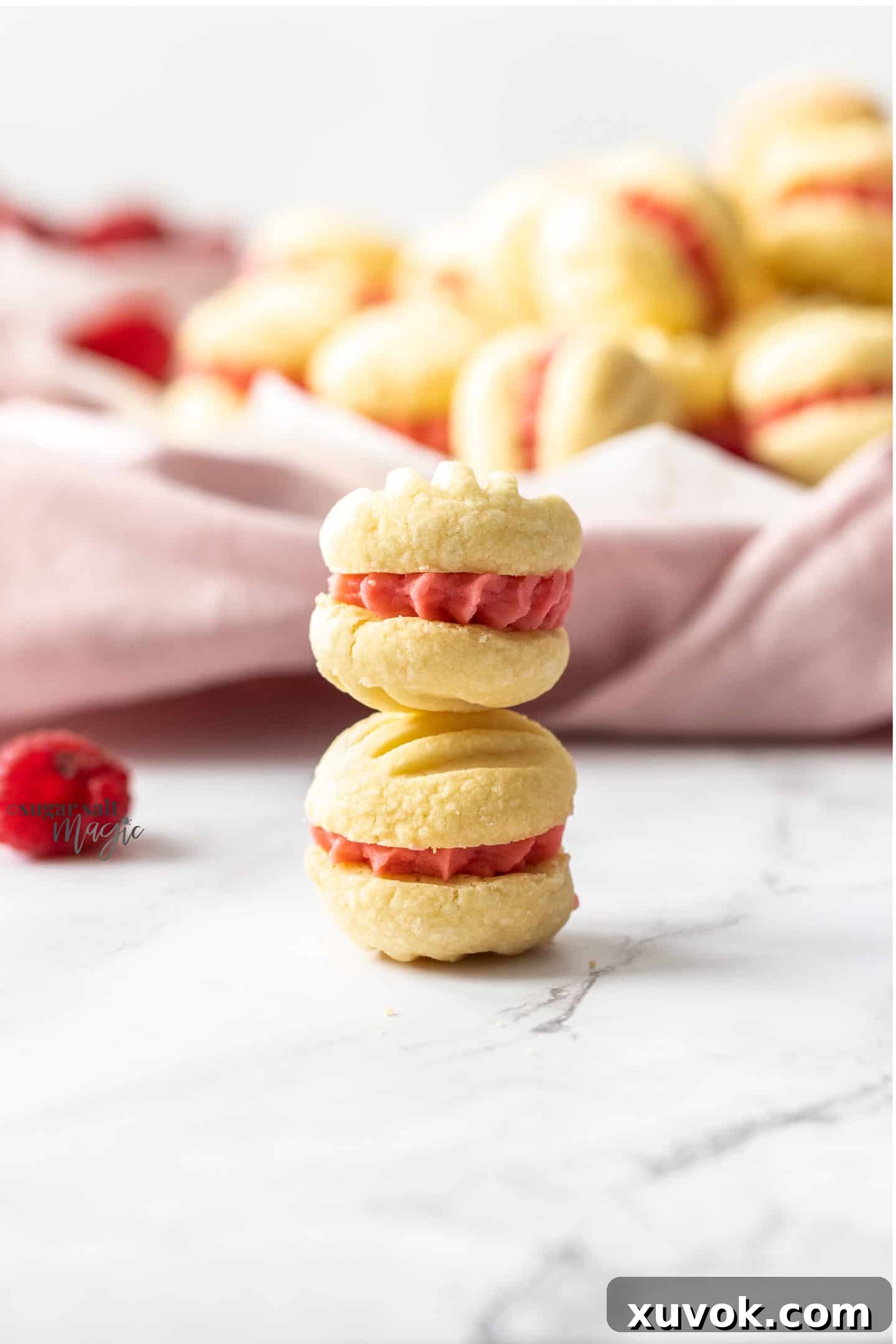 Two beautifully assembled Raspberry Melting Moments cookies, filled with vibrant pink buttercream, resting on a white marble countertop, showcasing their delicate texture.