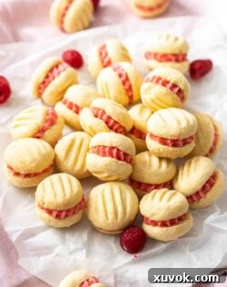 A charming stack of Raspberry Melting Moments cookies with a luscious raspberry buttercream filling, resting on a sheet of baking paper.