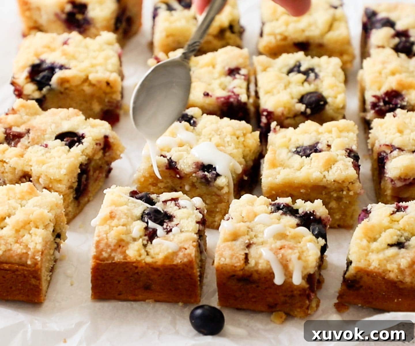 Lemon icing being drizzled over fudgy lemon blueberry bars with a crumb topping, creating a beautiful finish.
