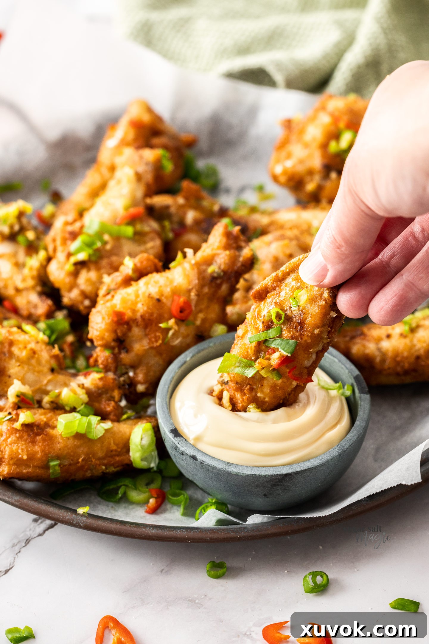 A hand dipping a chicken wing into mayonnaise.
