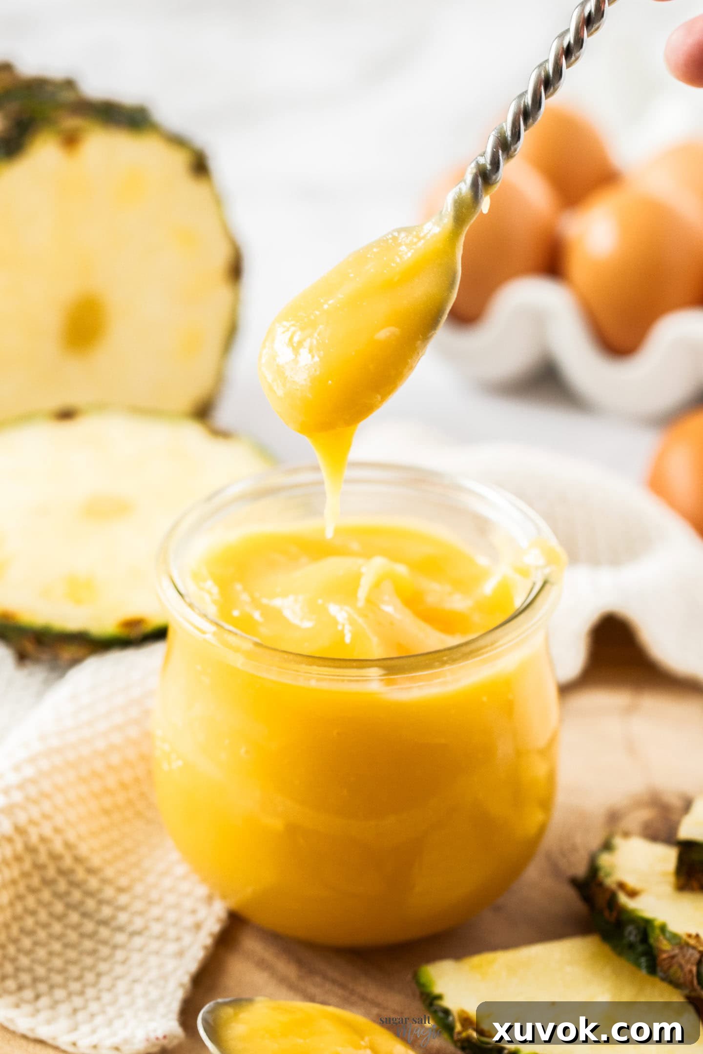 A spoon gracefully scooping a generous portion of pineapple curd from a glass jar.