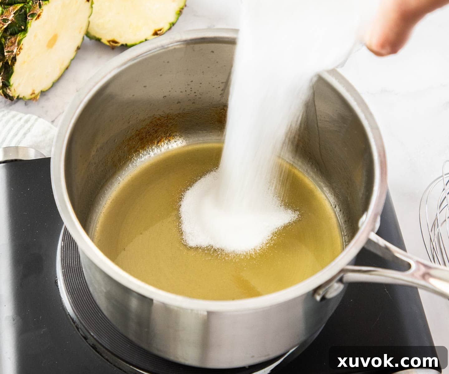 Sugar being added to the richly reduced pineapple juice in a saucepan.