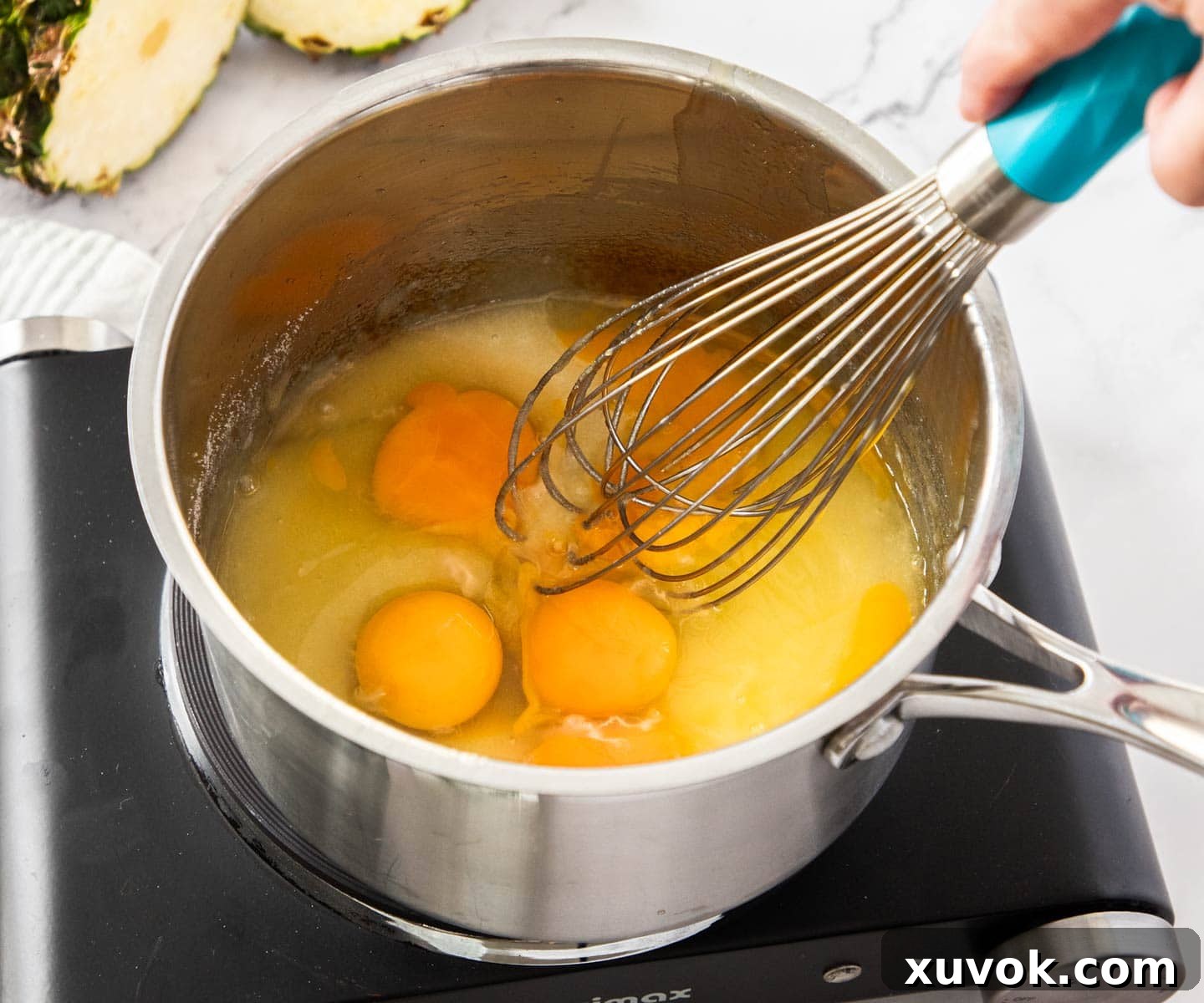 Eggs and sugar being whisked into the reduced pineapple juice mixture.