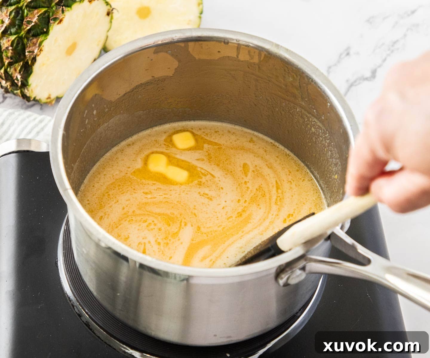 Cubed butter being gradually added to the saucepan with the pineapple curd mixture.