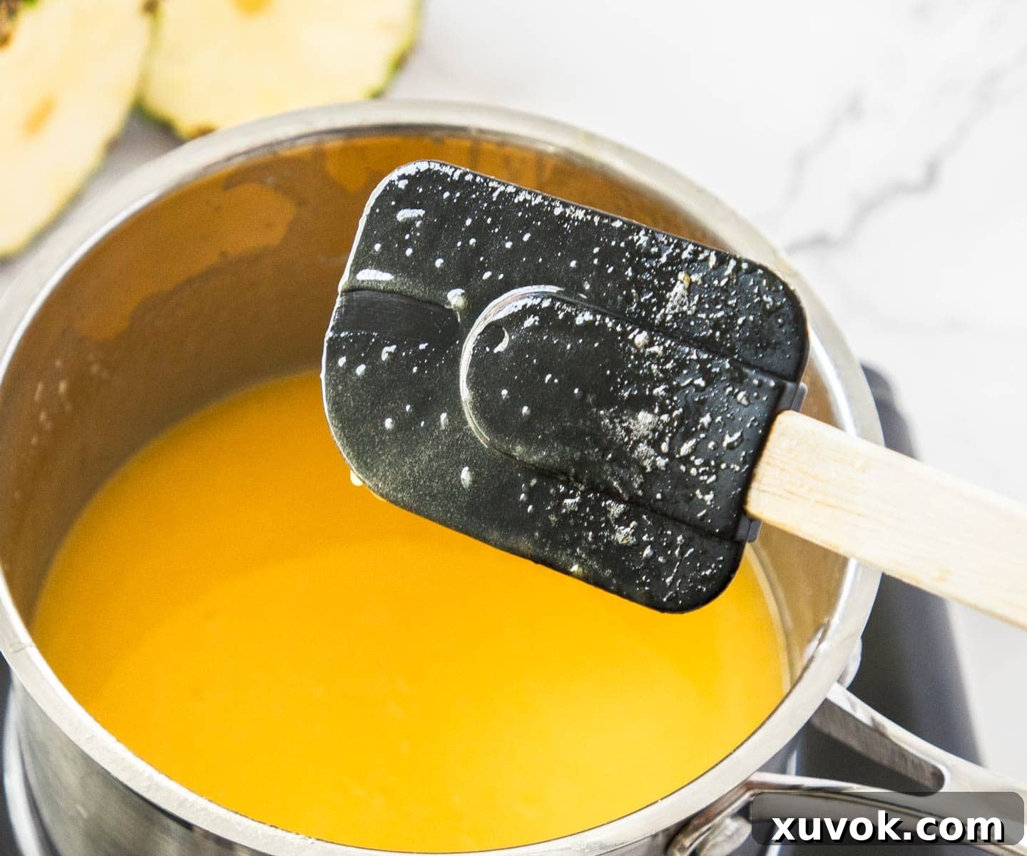 Close-up of a spatula with pineapple curd, showing a clear line drawn by a finger, indicating perfect thickness.
