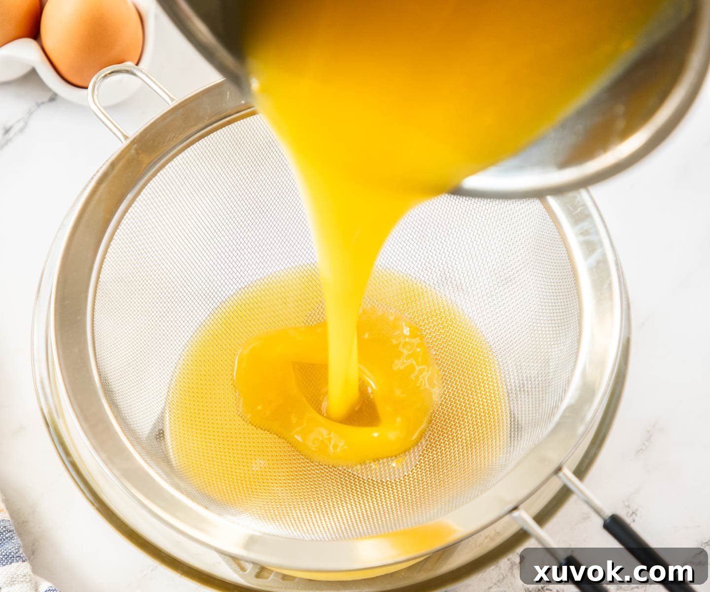 The hot pineapple curd being poured through a fine-mesh sieve into a glass bowl.
