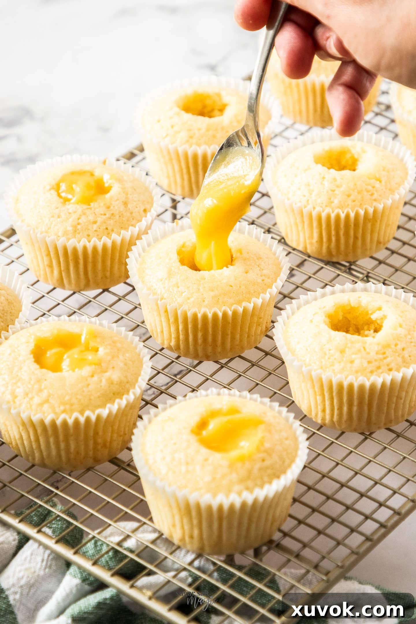 A spoon carefully dropping a dollop of creamy pineapple curd into the cored center of a cupcake.