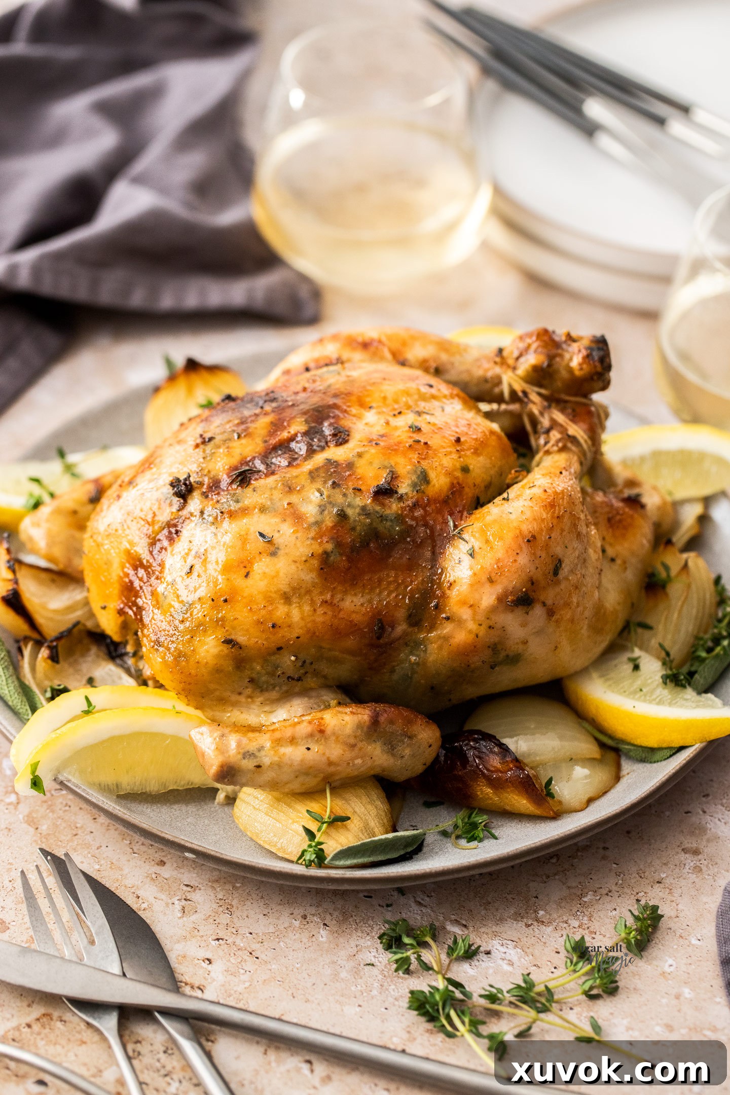 A beautifully roasted whole chicken presented on a serving plate, surrounded by roasted onions and ready to be carved.