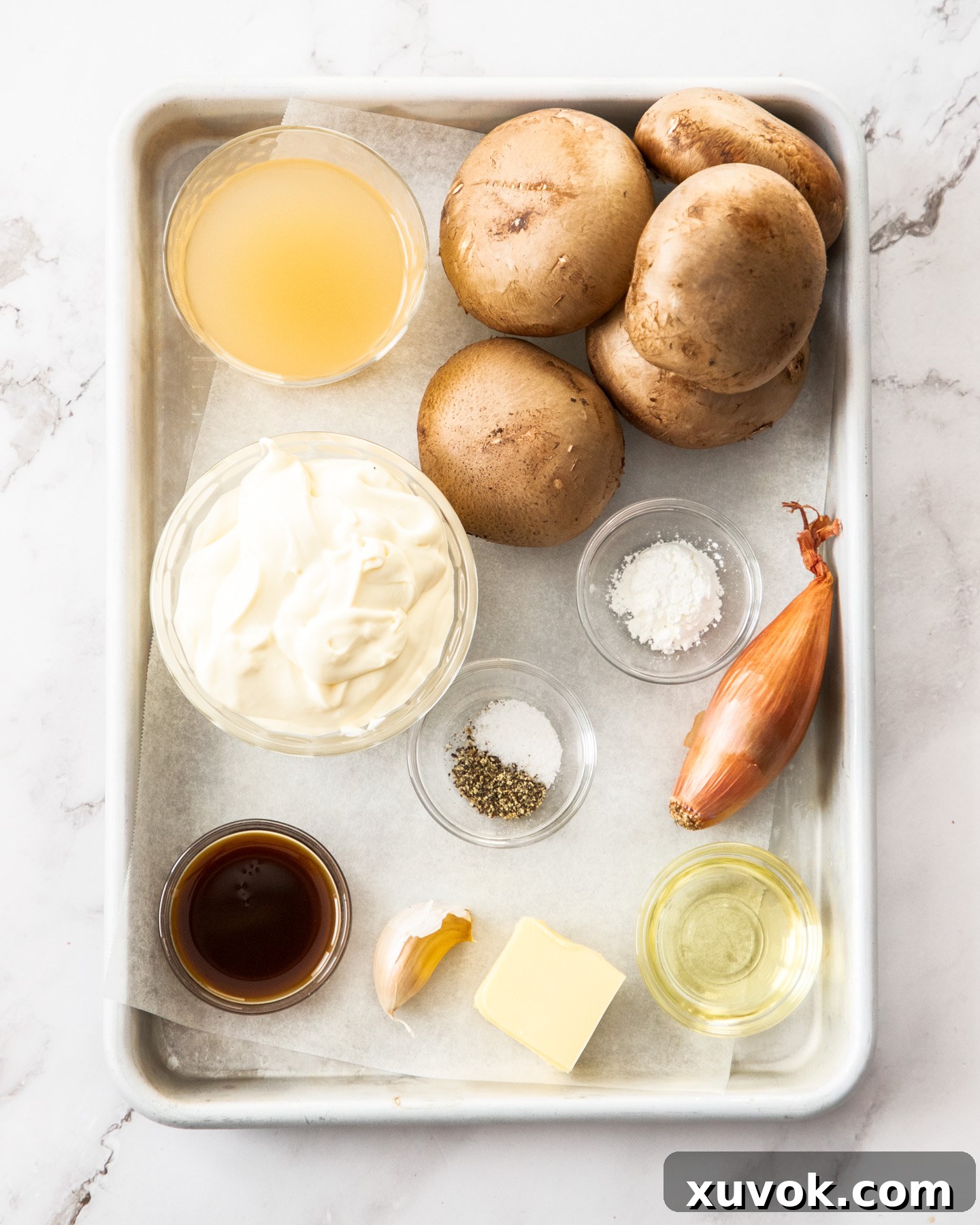 A selection of fresh ingredients including mushrooms, shallots, garlic, butter, and cream, arranged on a baking tray, ready for making creamy mushroom sauce.