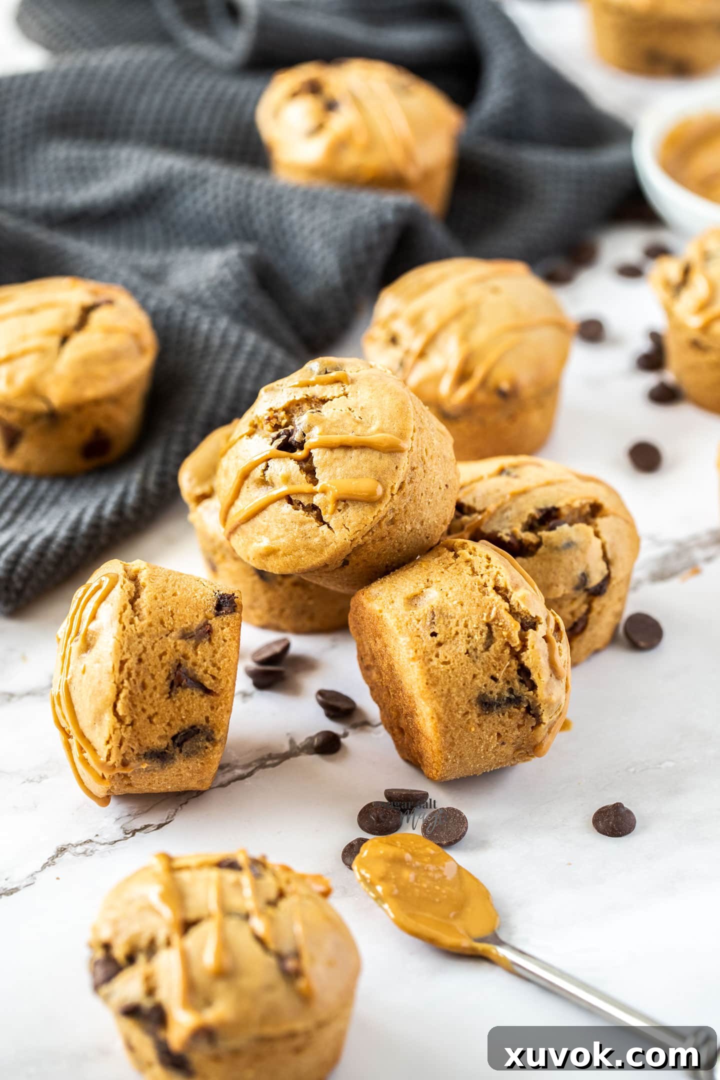 Stacked peanut butter chocolate chip muffins with loose chocolate chips and peanuts