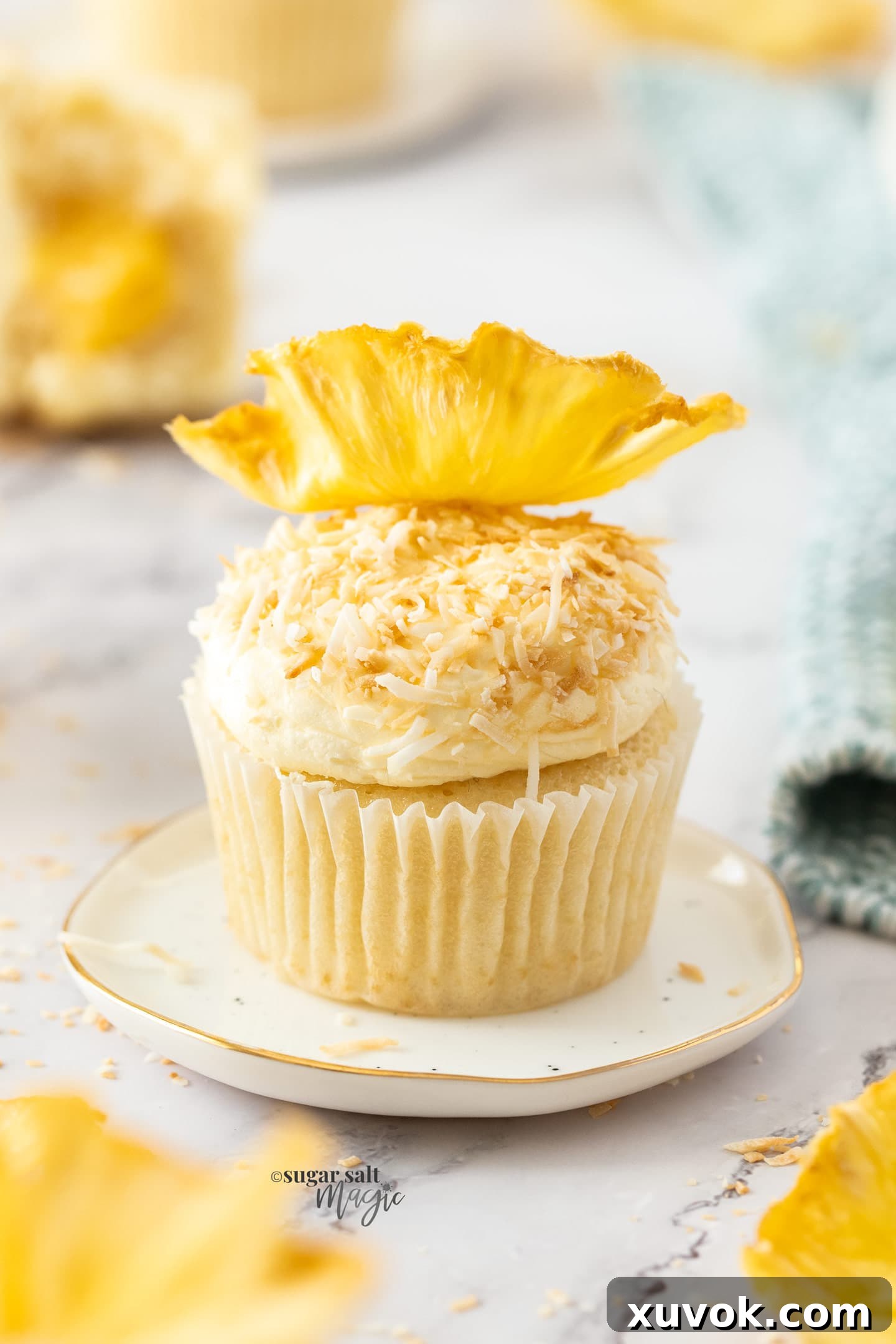 Closeup of a pineapple coconut cupcake, generously coated with toasted coconut and adorned with a delicate dried pineapple flower, inviting you to a tropical taste experience.