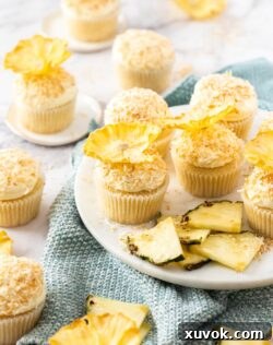 A batch of pineapple coconut cupcakes, beautifully decorated with creamy frosting, toasted coconut, and elegant dried pineapple flowers.