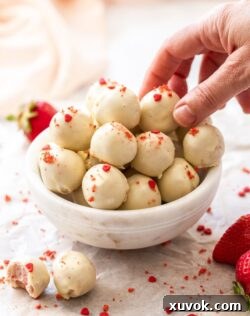 A batch of white chocolate truffles in a small white bowl with a hand reaching into pick one up