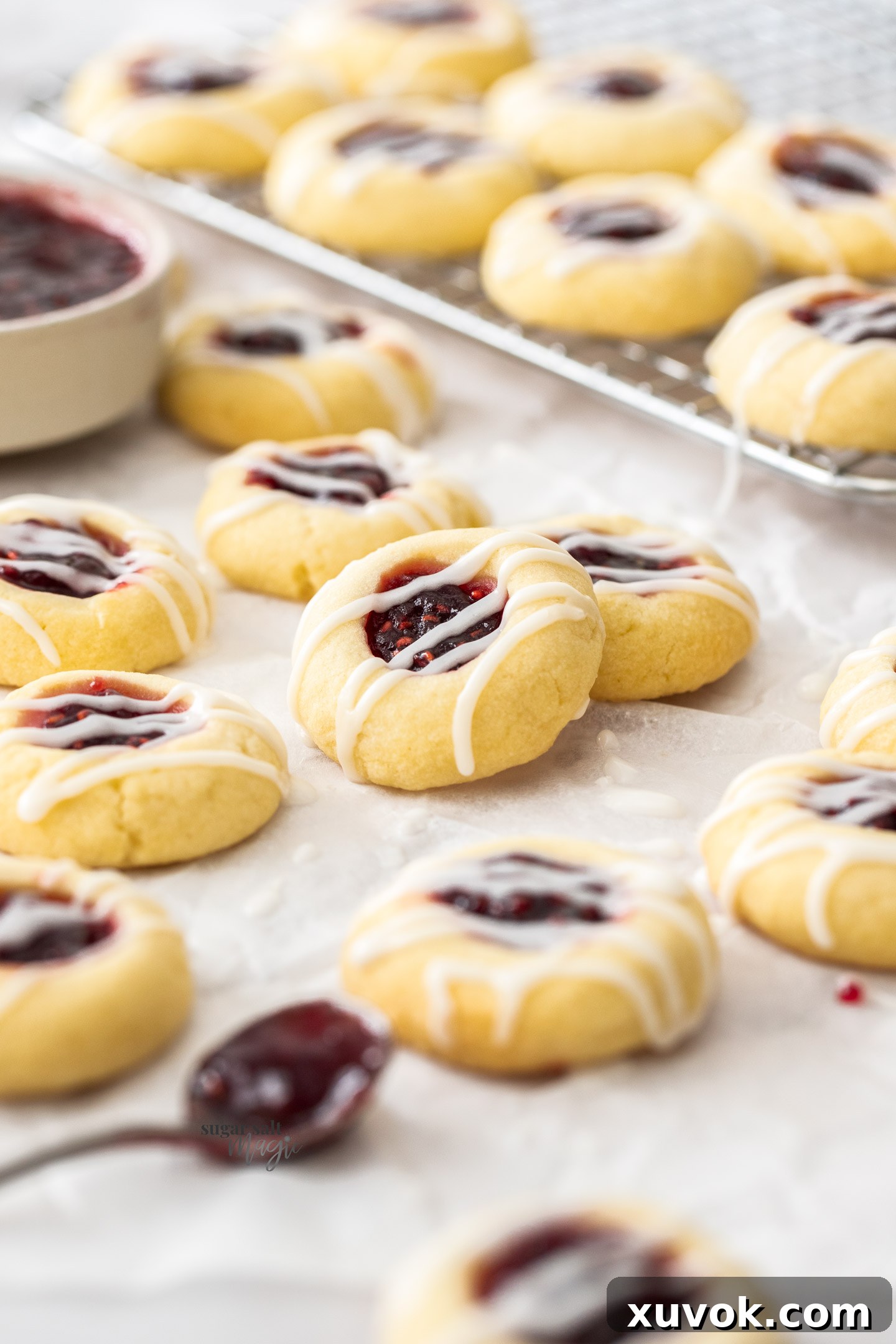 A batch of jam thumbprint cookies on a sheet of baking paper.