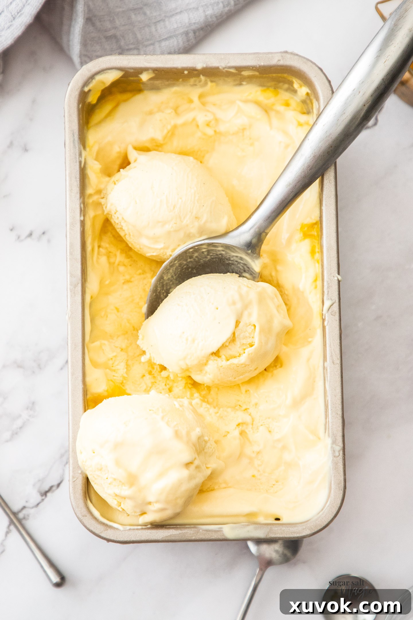Top down view of vibrant yellow passion fruit ice cream in a white loaf pan, garnished with fresh passion fruit halves and mint leaves, highlighting its creamy texture.