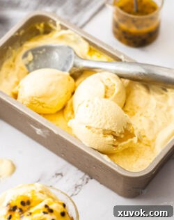 A close-up image of creamy passion fruit ice cream in a white loaf pan, partially scooped, showcasing its smooth texture and vibrant color.